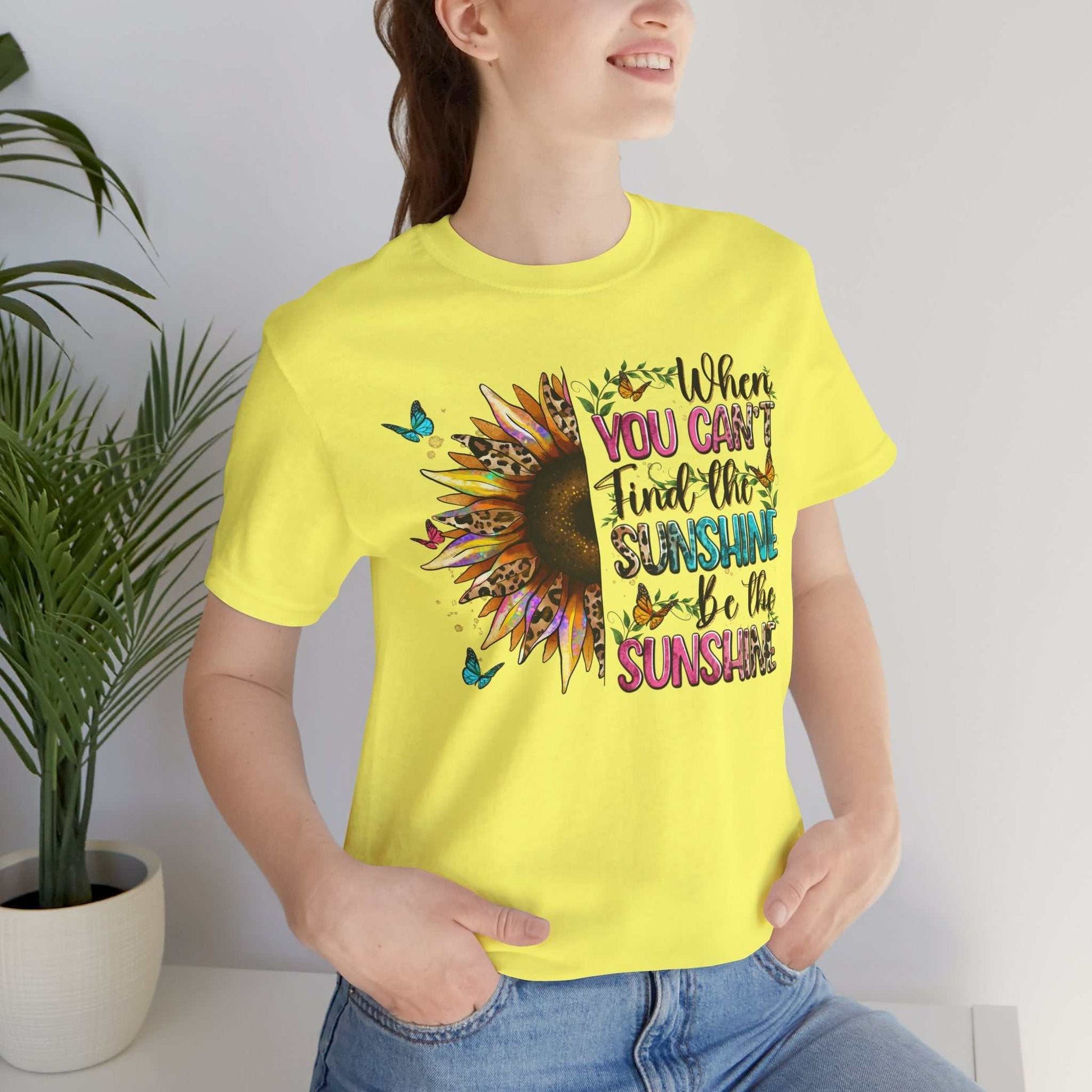 Woman wearing yellow Sunshine Quote Tee with sunflower and motivational text design standing indoors