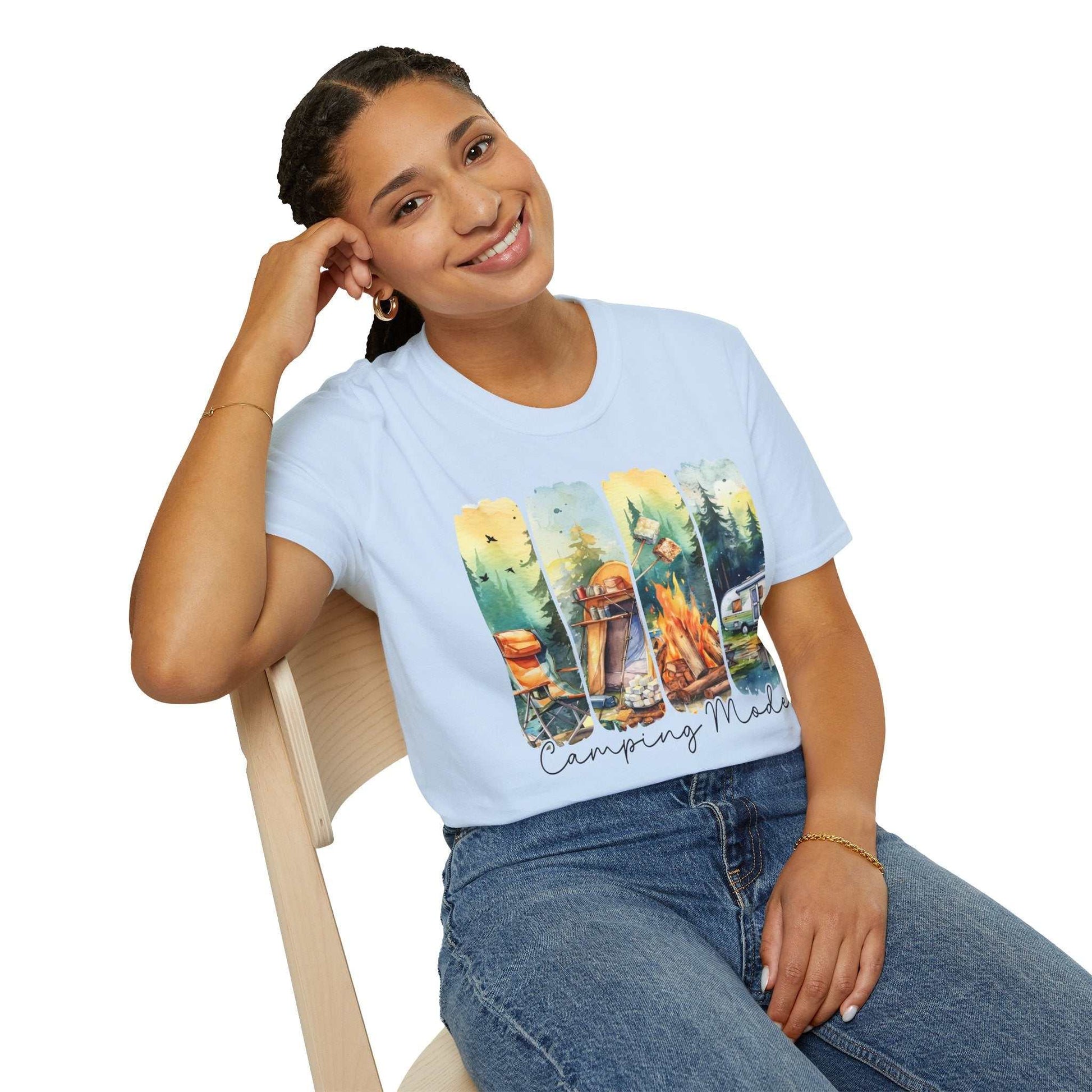 Woman wearing light blue Camping Adventure Unisex T-Shirt with camping scene graphic, sitting on chair and smiling