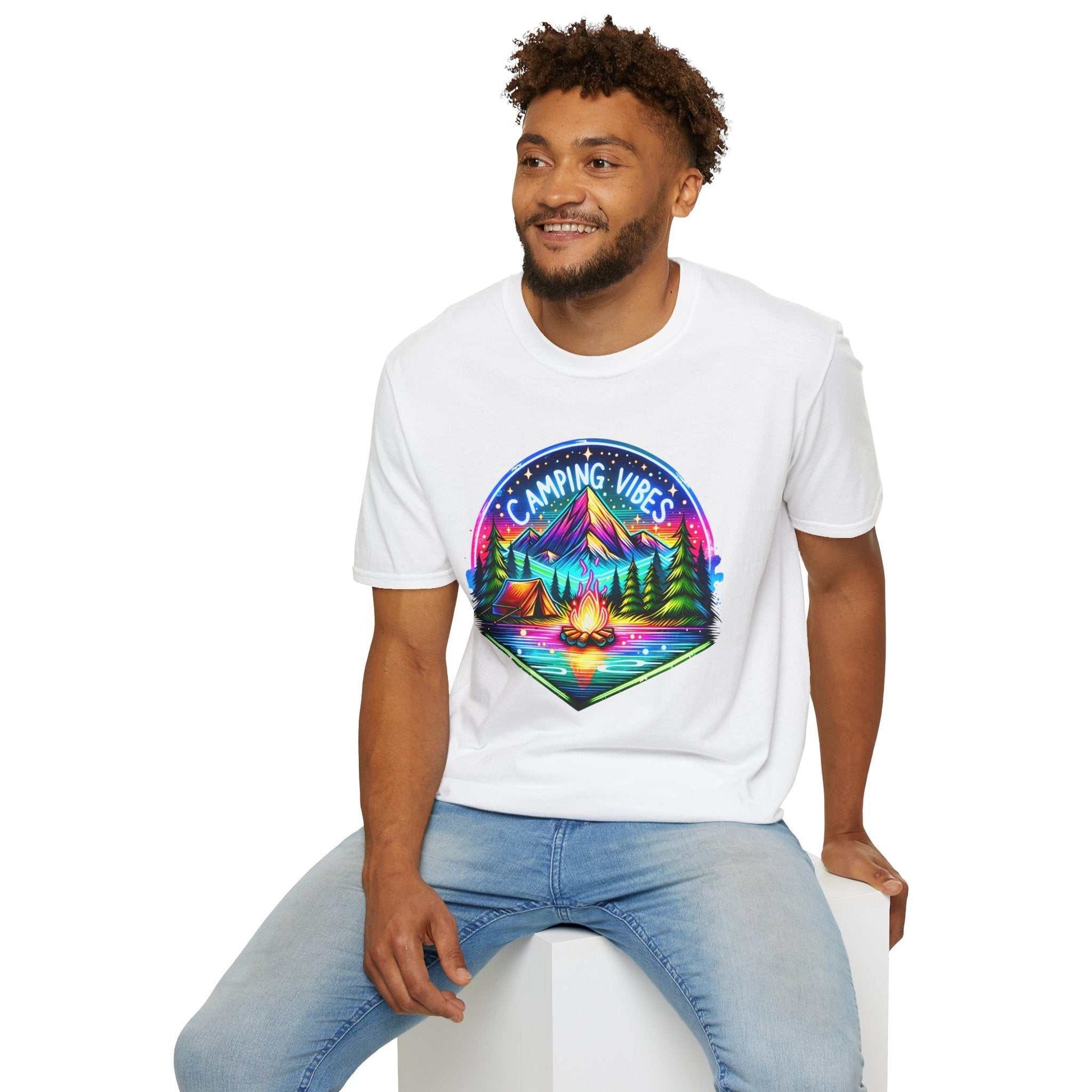 Man wearing white Camping Vibes Unisex Softstyle T-Shirt with colorful camping graphic logo sitting on white cube