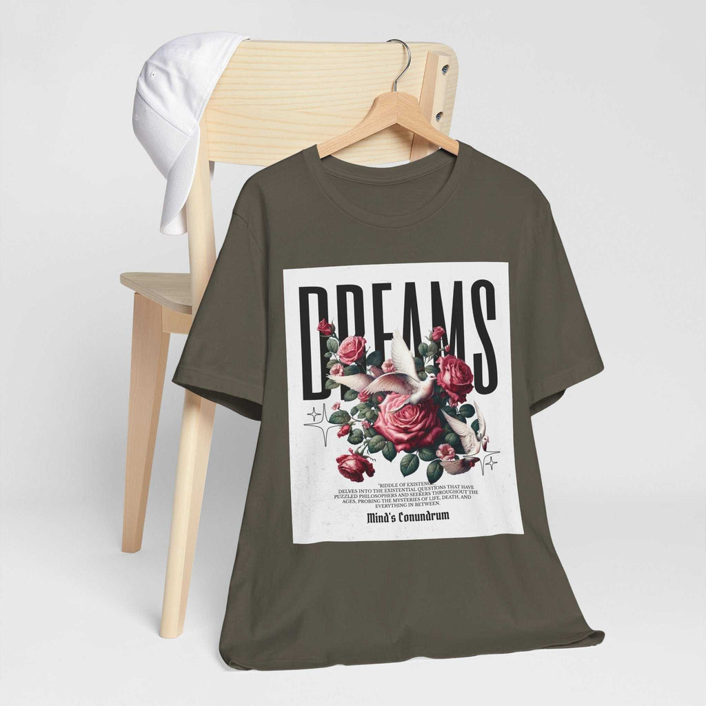 Unisex Dreams Floral Tee with bold typography and floral design on olive green fabric hanging on wooden hanger with white cap on chair.