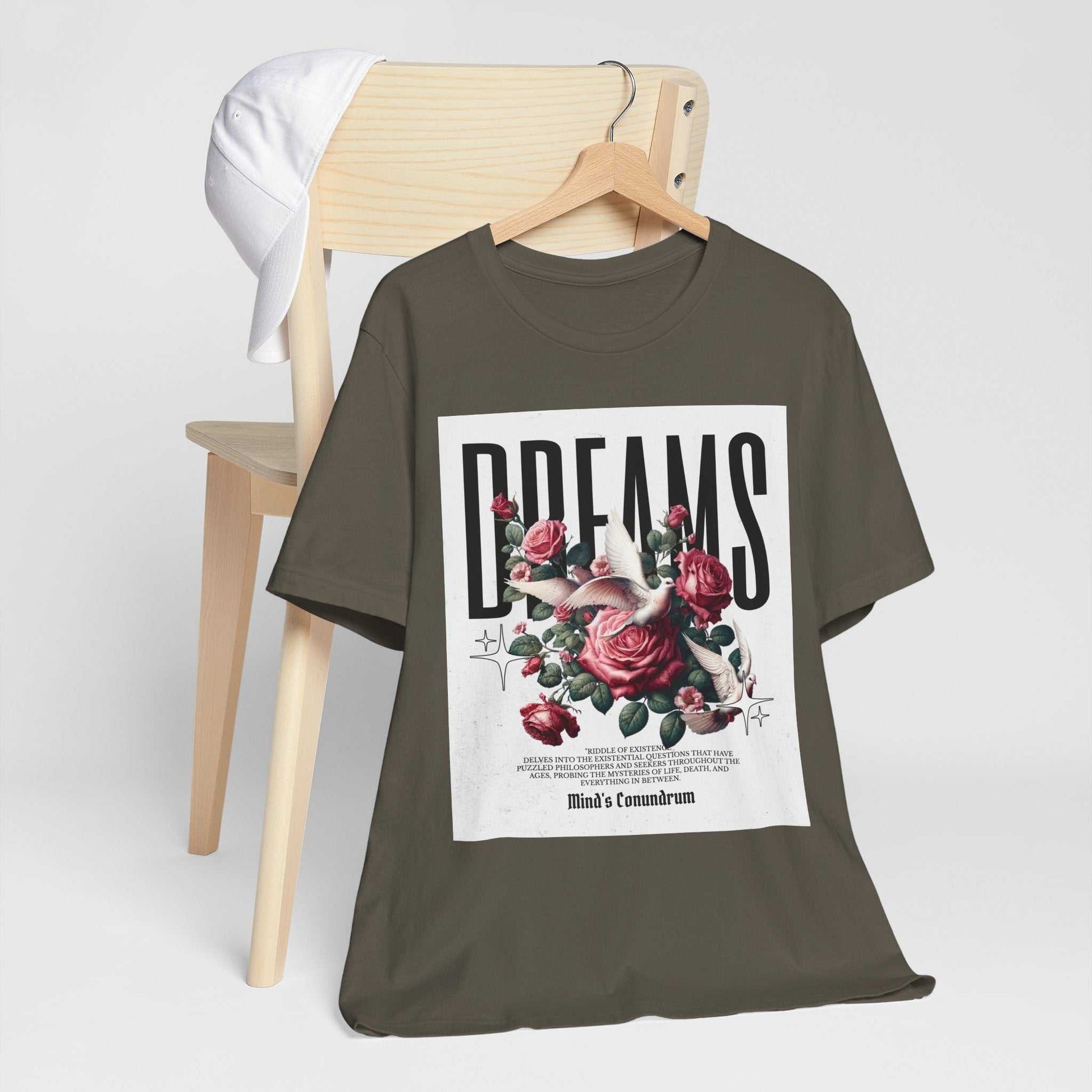 Unisex Dreams Floral Tee with bold typography and floral design on olive green fabric hanging on wooden hanger with white cap on chair.