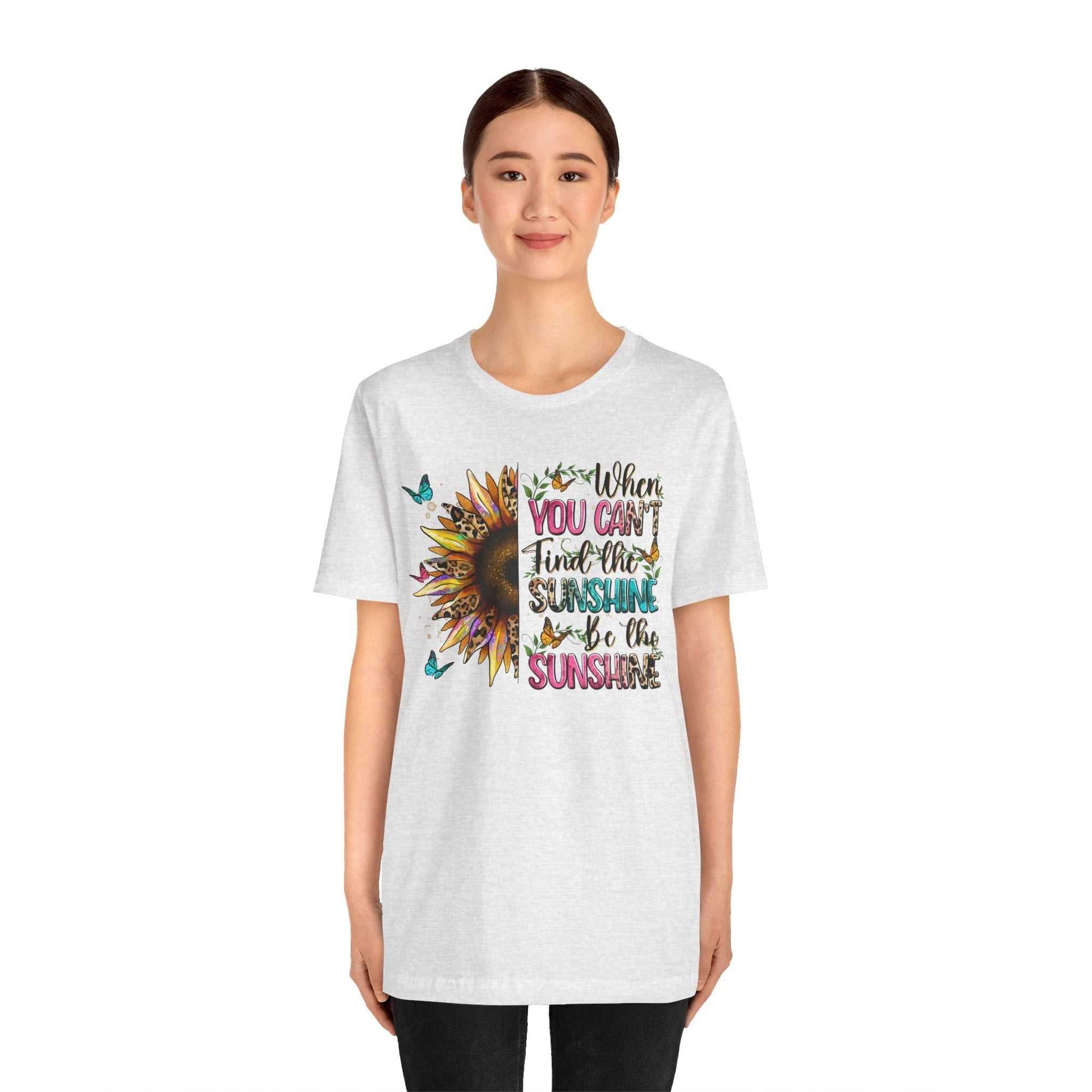 Woman wearing white Sunshine Quote Tee with colorful sunflower and text design reading "When you can't find the sunshine be the sunshine"
