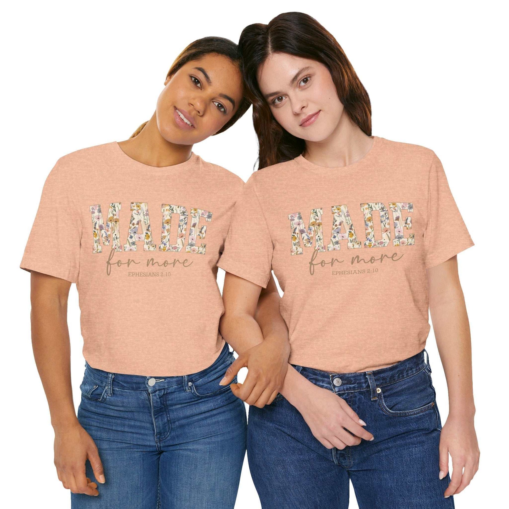Two women wearing peach-colored "Made for More" unisex jersey short sleeve tees with floral lettering and casual denim jeans