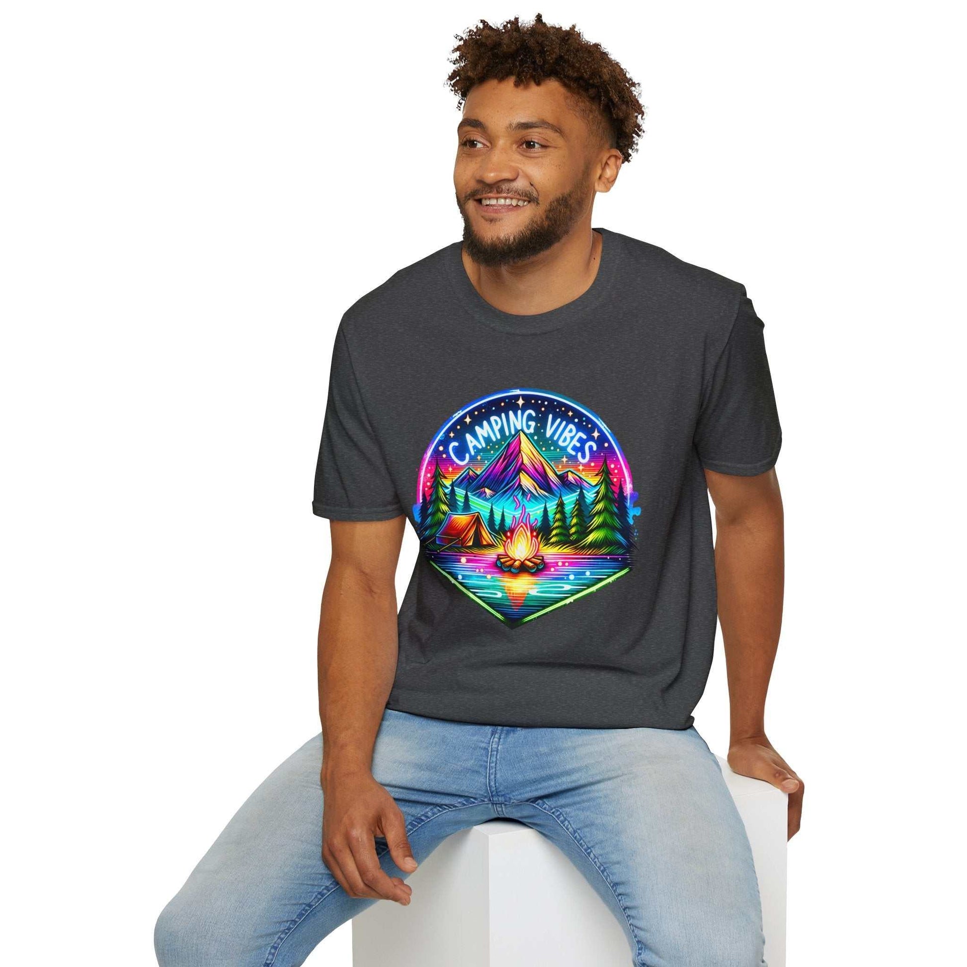 Man wearing dark Camping Vibes Unisex softstyle t-shirt with colorful mountain and campfire design sitting on white cube