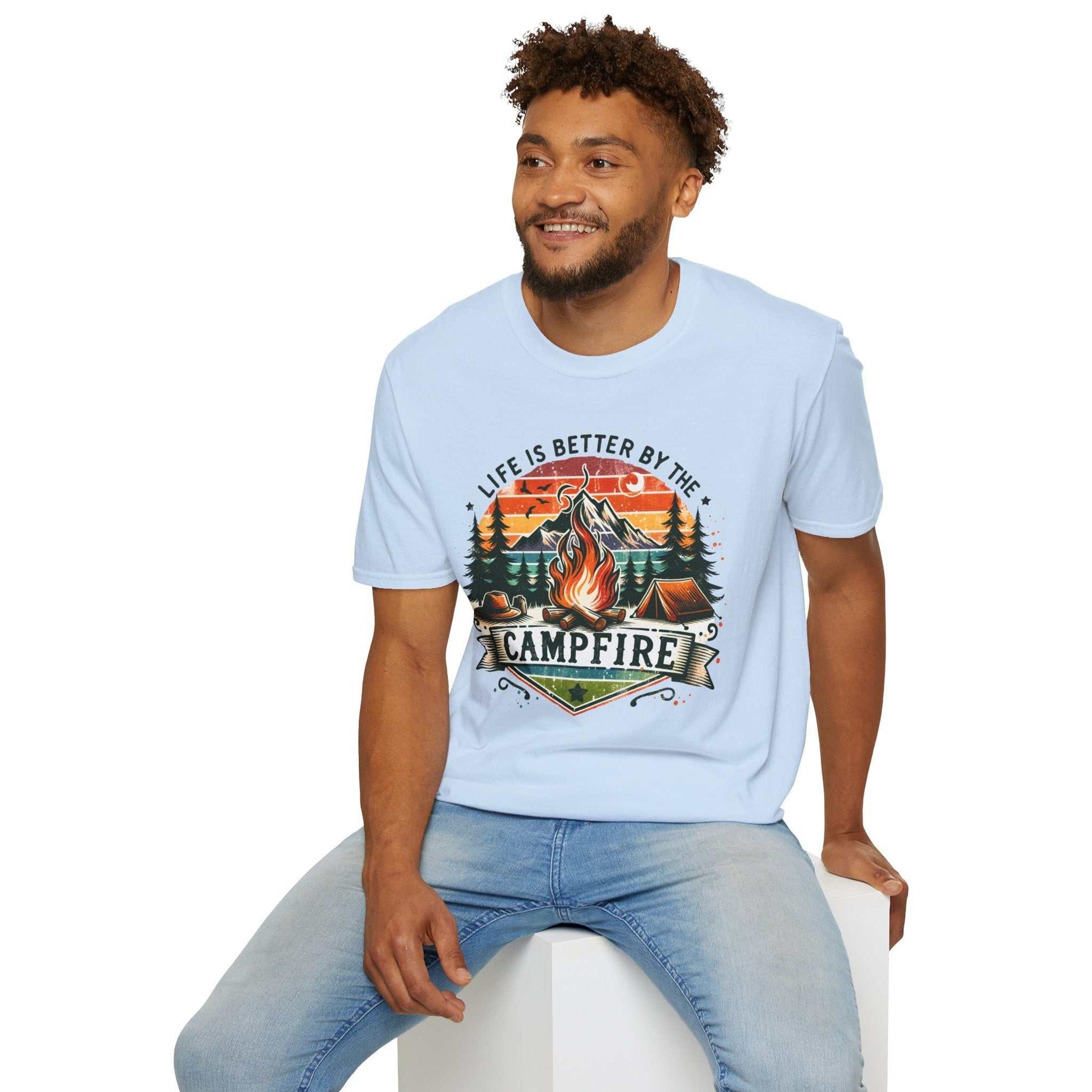 Man wearing light blue unisex Camping Adventure T-shirt with "Life is Better by the Campfire" graphic and campfire design.