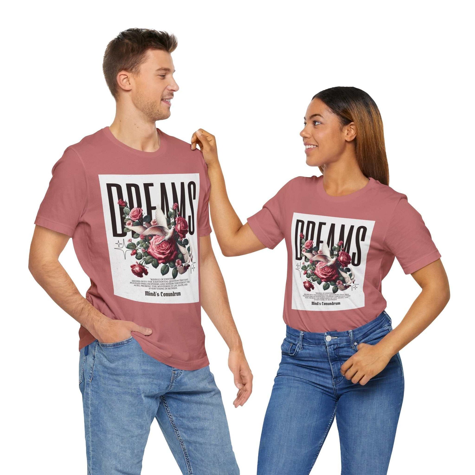 Unisex Dreams Floral Tee with pink background, bold typography, and floral graphic, worn casually by man and woman in jeans.
