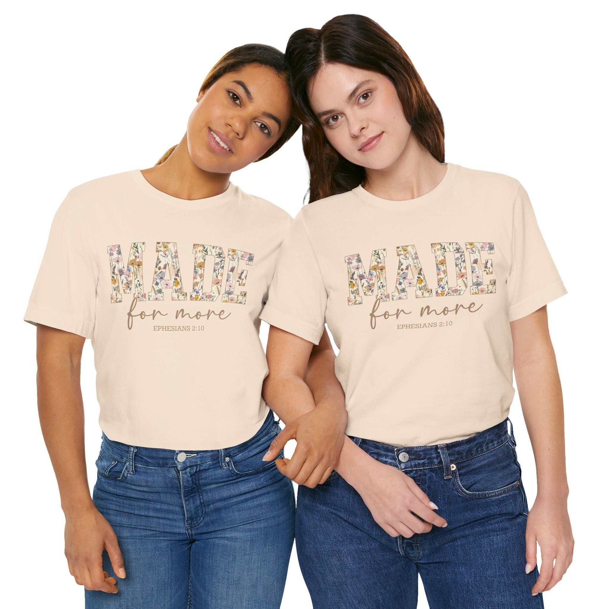 Two women wearing beige "Made for More" unisex short sleeve tees with floral print lettering, styled casually with jeans.