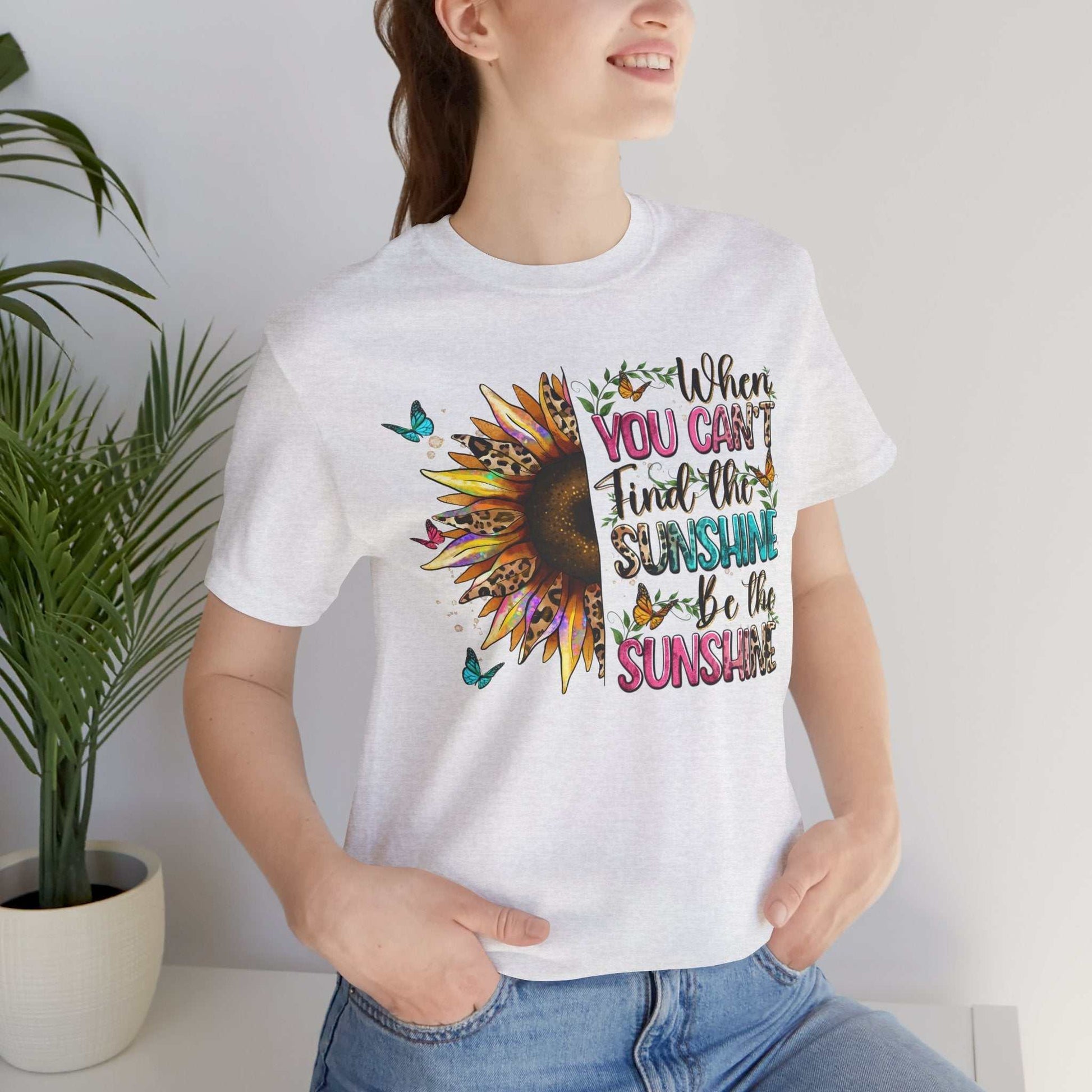 Woman wearing white Sunshine Quote Tee with colorful sunflower and uplifting text design