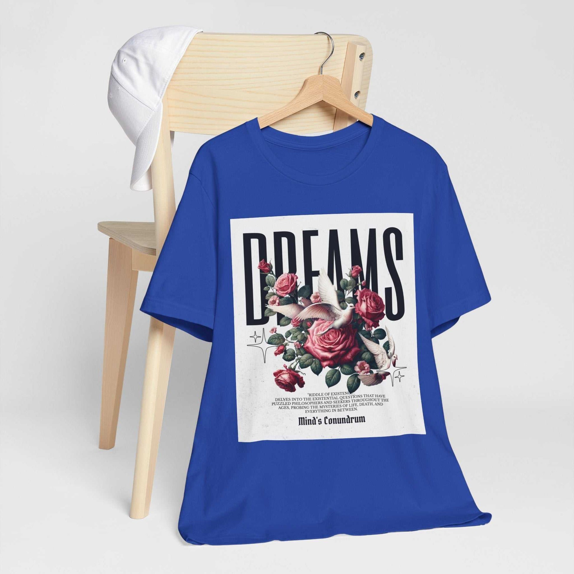 Blue Dreams Floral Tee with bold typography and pink rose graphic on front displayed on a wooden chair with white baseball cap