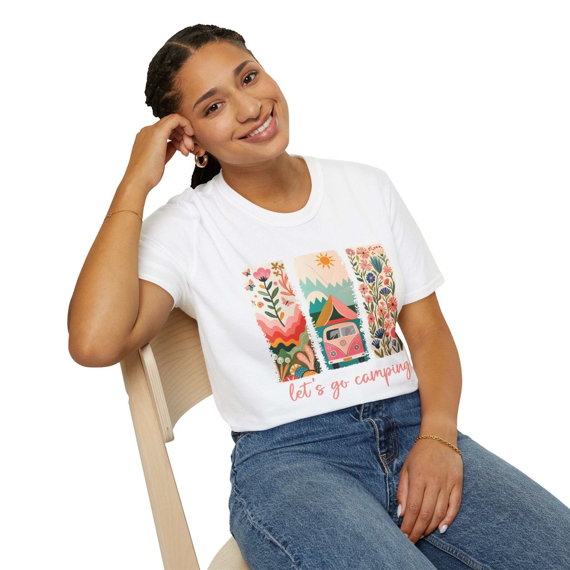 Woman wearing white Camping Adventure unisex softstyle t-shirt with colorful camping-themed design and "let's go camping" text sitting on wooden chair.