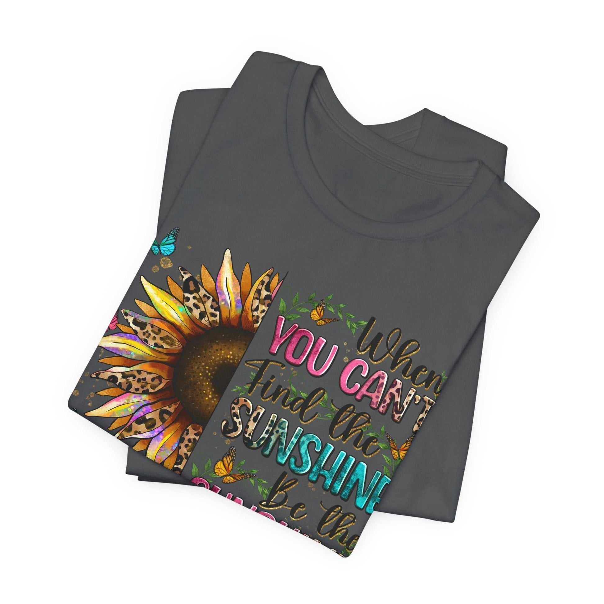 Folded dark grey Sunshine Quote Tee featuring colorful sunflower and butterfly design with the inspirational text "When you can't find the sunshine be the sunshine"