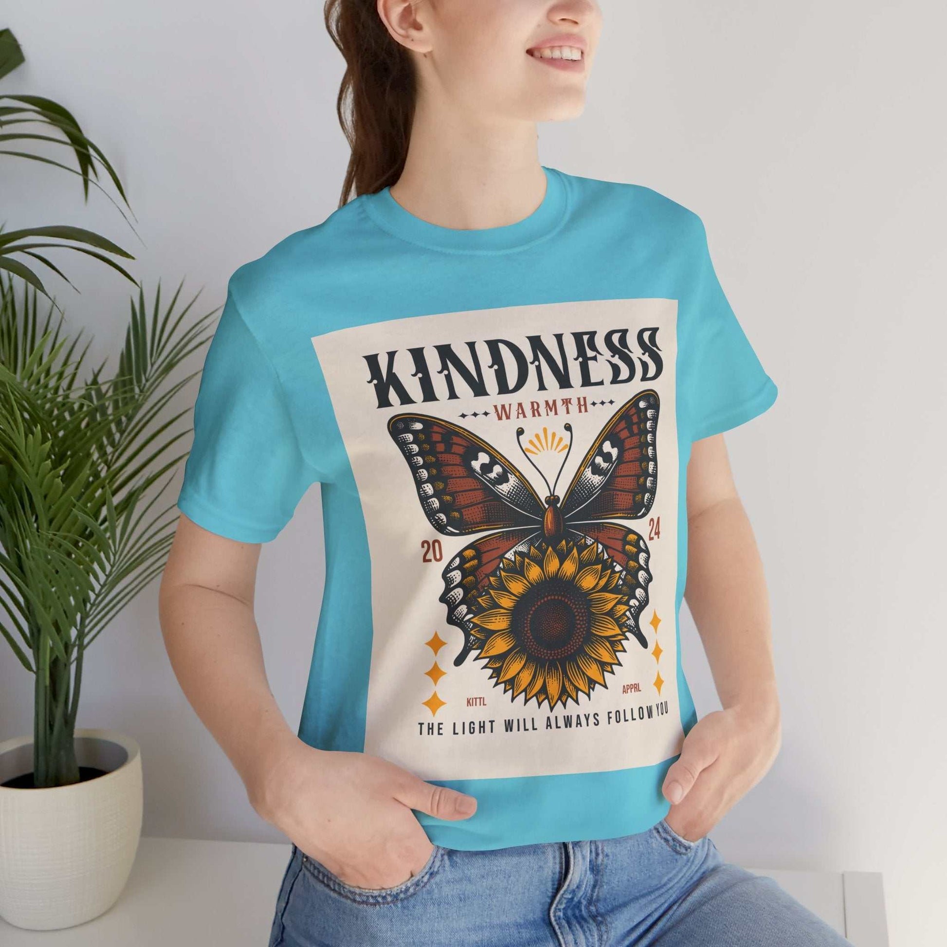 Woman wearing light blue Kindness Butterfly Tee with butterfly and sunflower design and text "Kindness Warmth The Light Will Always Follow"