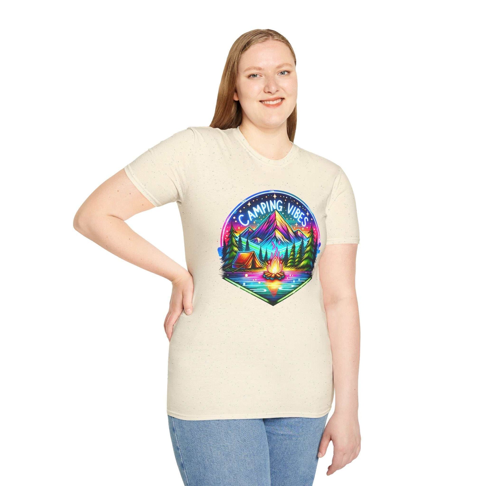 Woman wearing a beige unisex softstyle t-shirt with colorful "Camping Vibes" graphic featuring mountains, a campfire, and tents