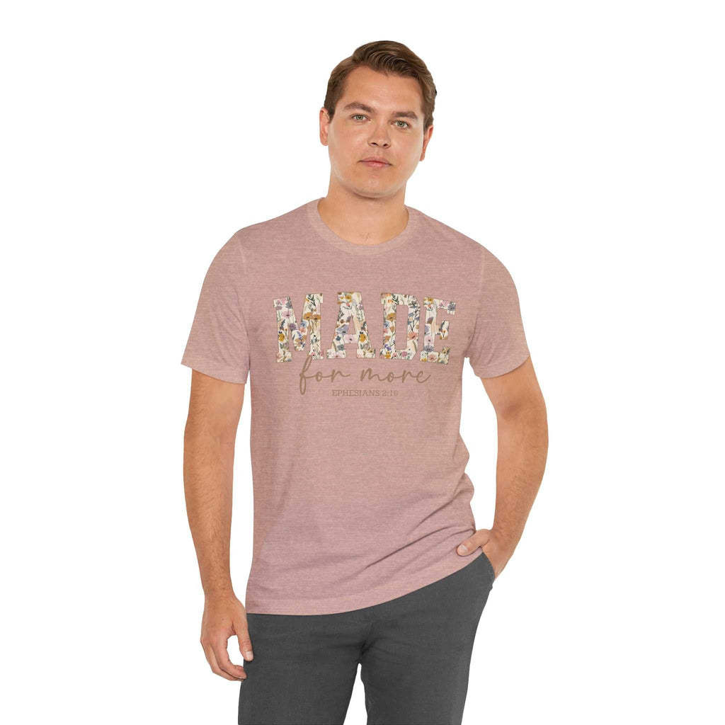 Man wearing a pink Made for More Tee with floral lettering on front and casual black pants.