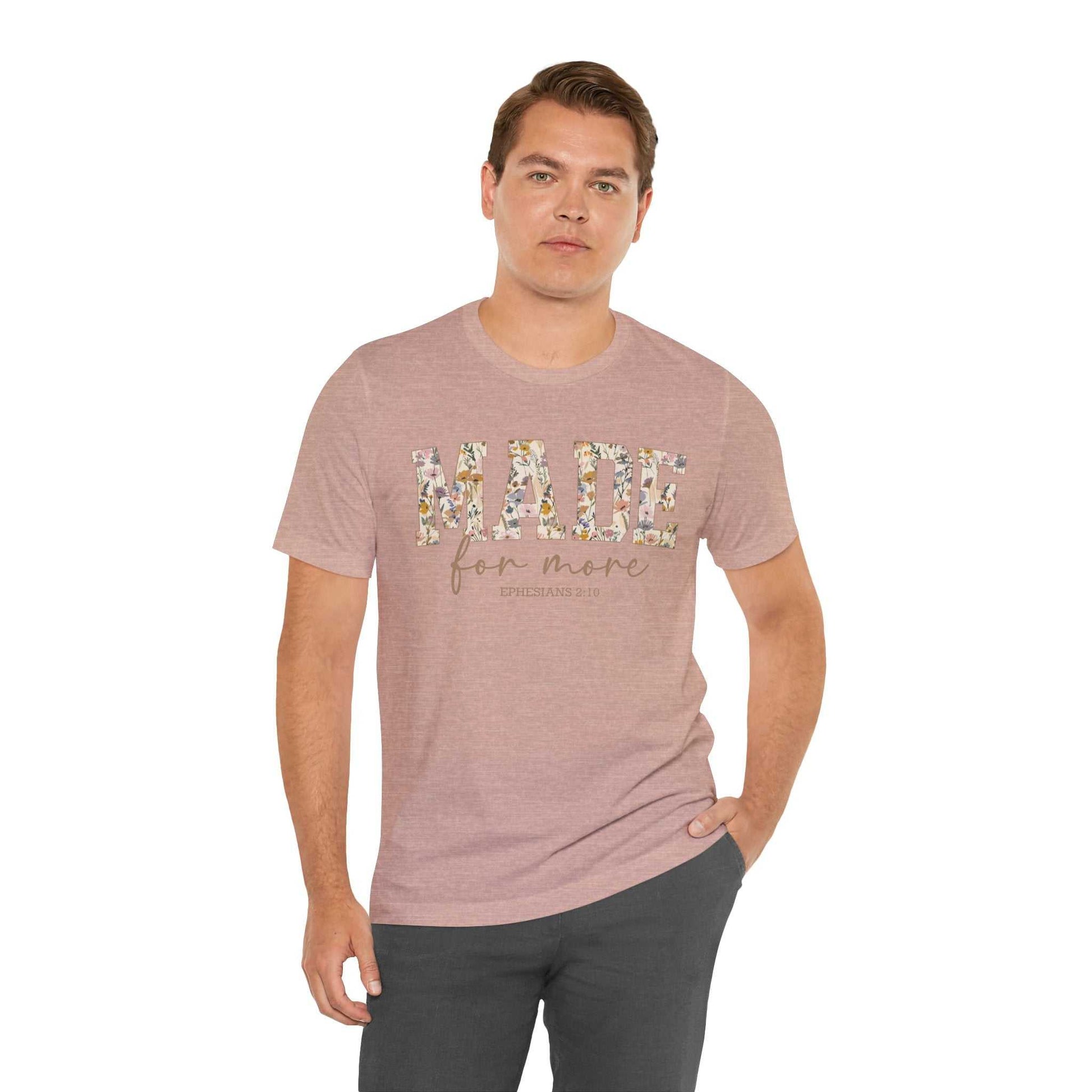 Man wearing a pink Made for More Tee with floral lettering on front and casual black pants.