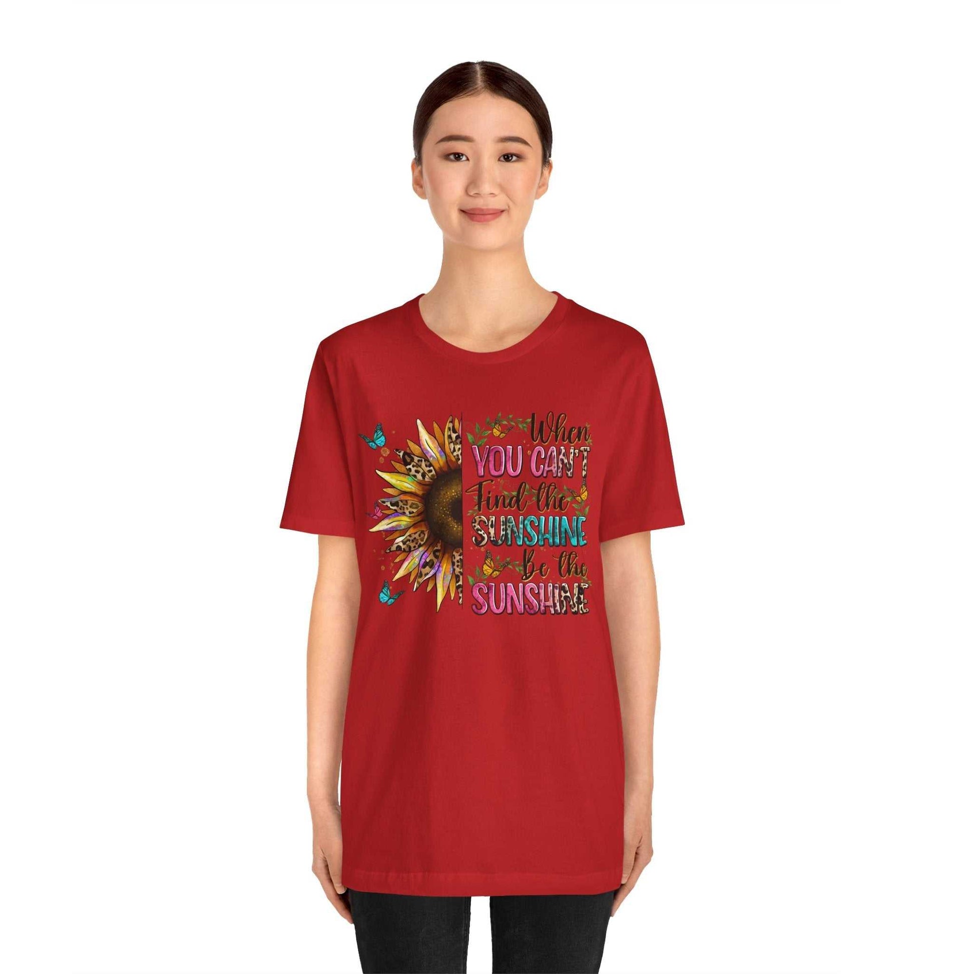 Woman wearing a red Sunshine Quote Tee with a vibrant sunflower and colorful text design on the front.