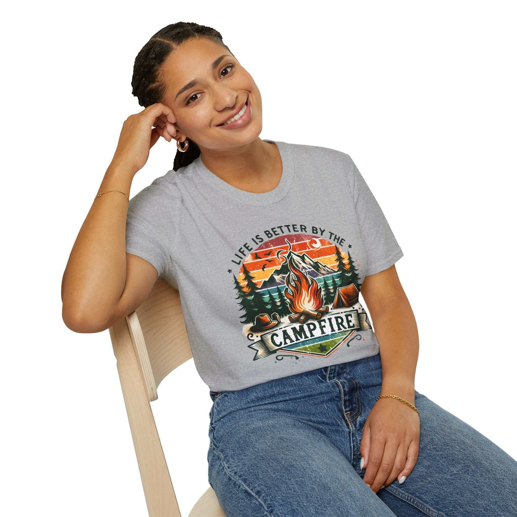 Woman wearing grey Camping Adventure Unisex T-Shirt with campfire graphic and "Life is Better by the Campfire" text, sitting on chair.