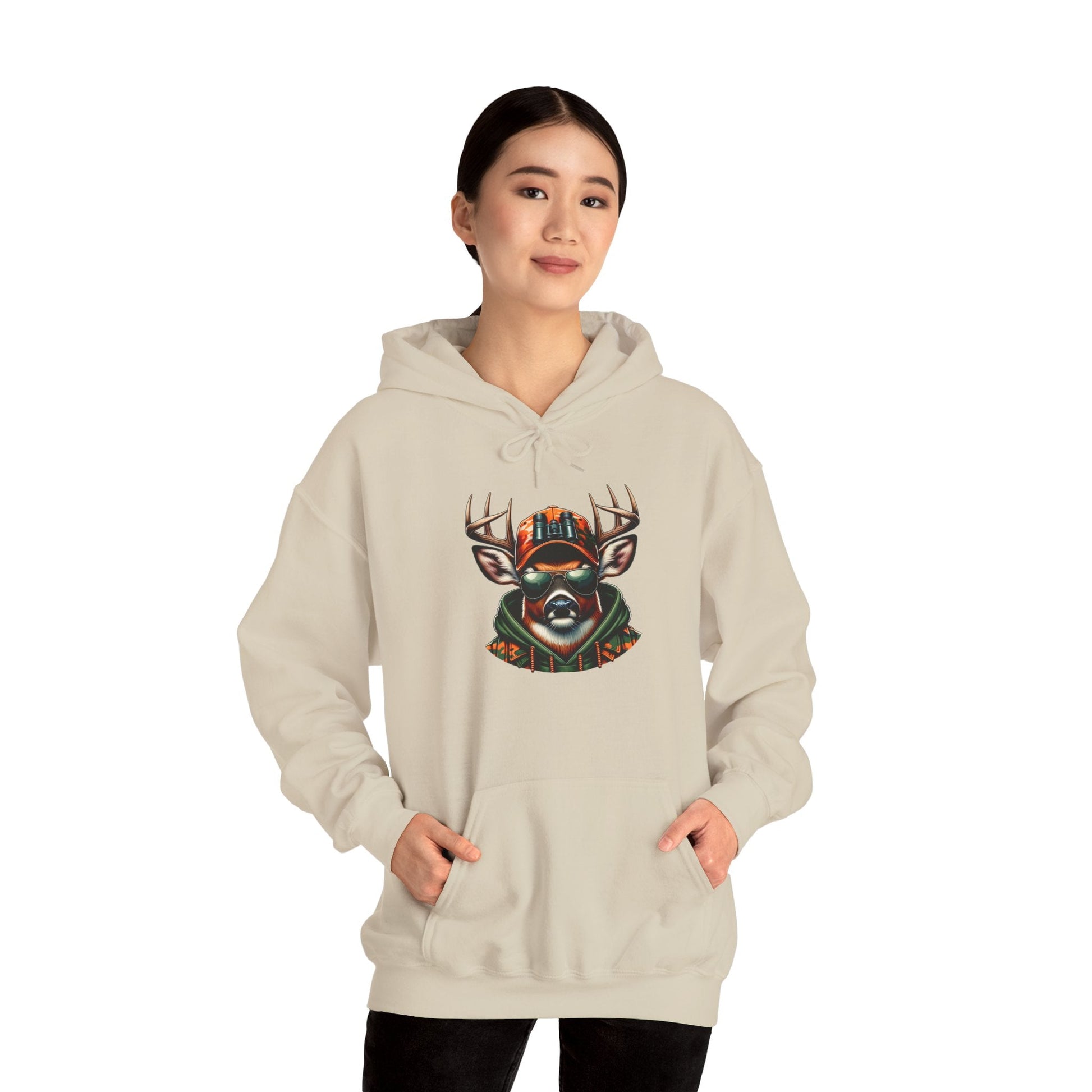 Woman wearing beige hooded sweatshirt featuring bold deer design with antlers and cap, hands in kangaroo pouch pocket.