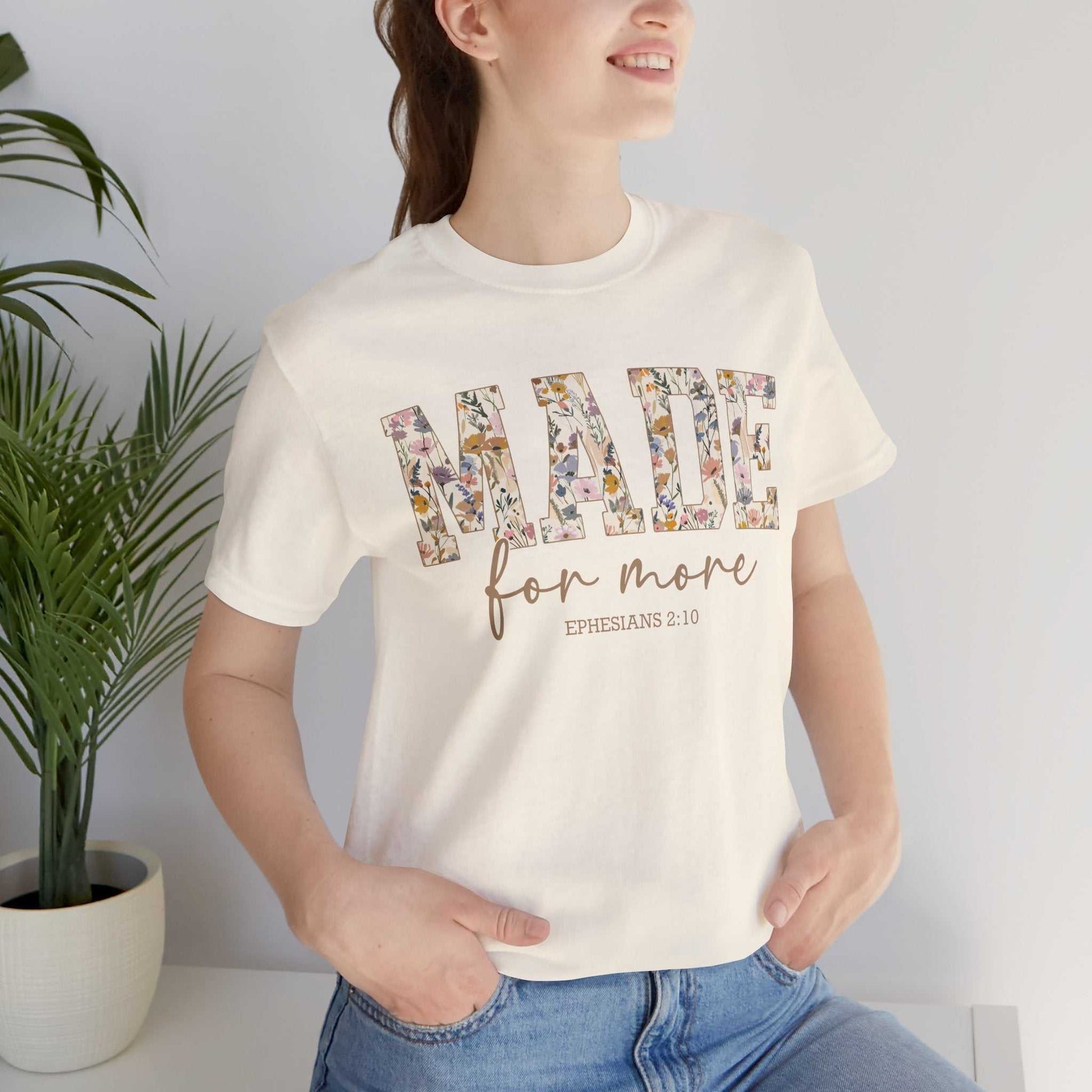 Woman wearing Made for More Tee with floral text design and scripture reference Ephesians 2:10 in casual setting