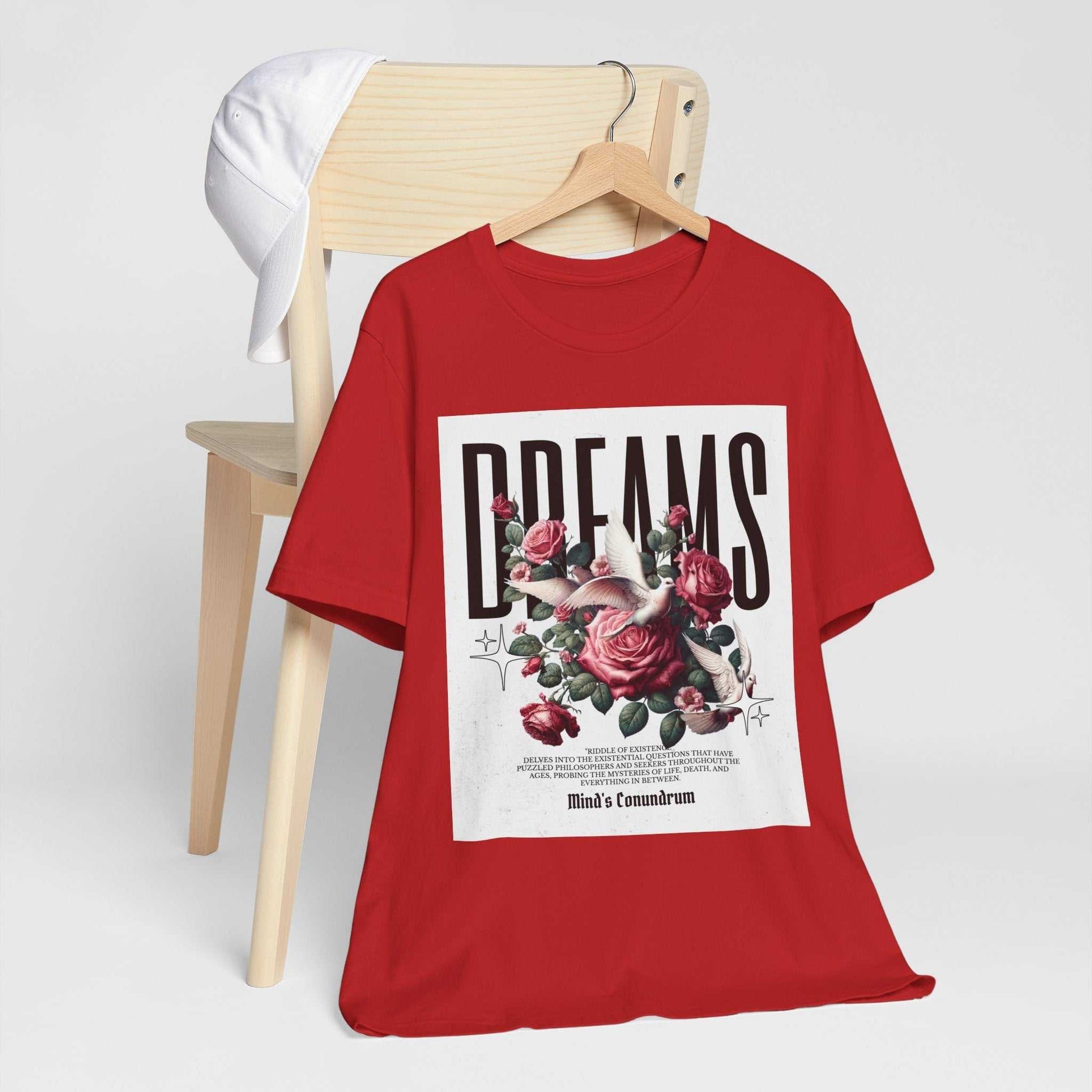 Red Dreams Floral Tee with bold typography and rose graphic design on front, displayed on wooden chair with white cap.