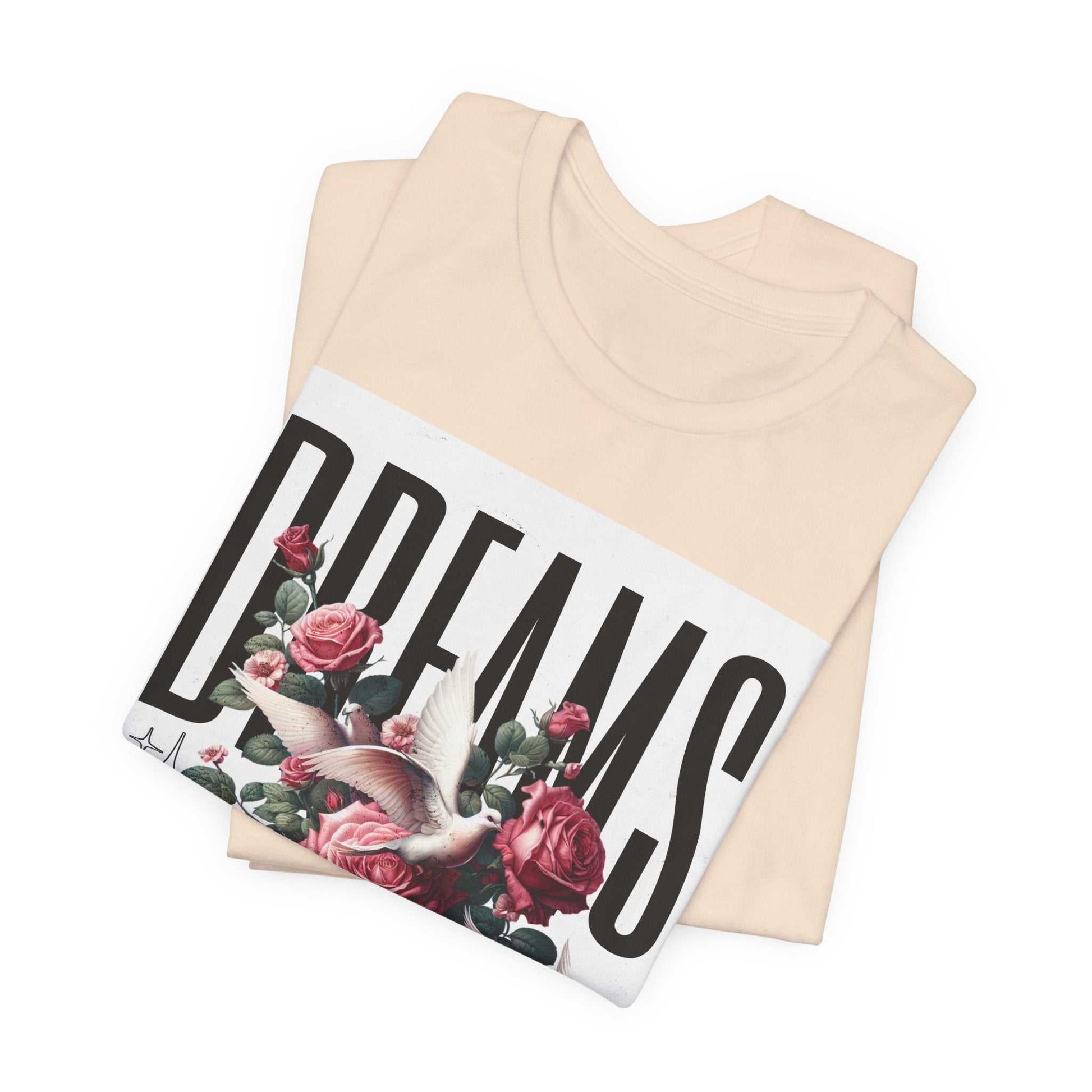 Folded cream-colored Dreams Floral Tee with bold black "DREAMS" text, pink roses, and a white dove graphic on front