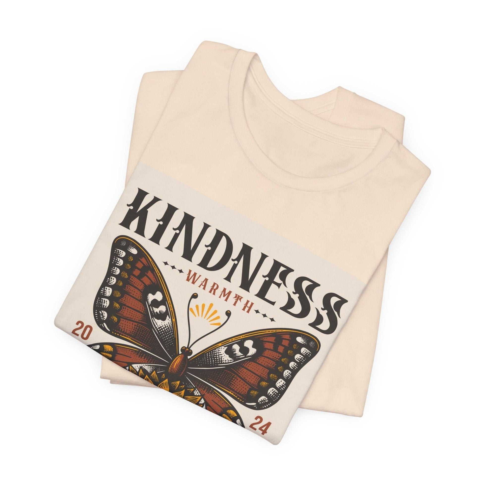 Folded beige Kindness Butterfly Tee with butterfly graphic and "KINDNESS WARMTH 2024" text on front