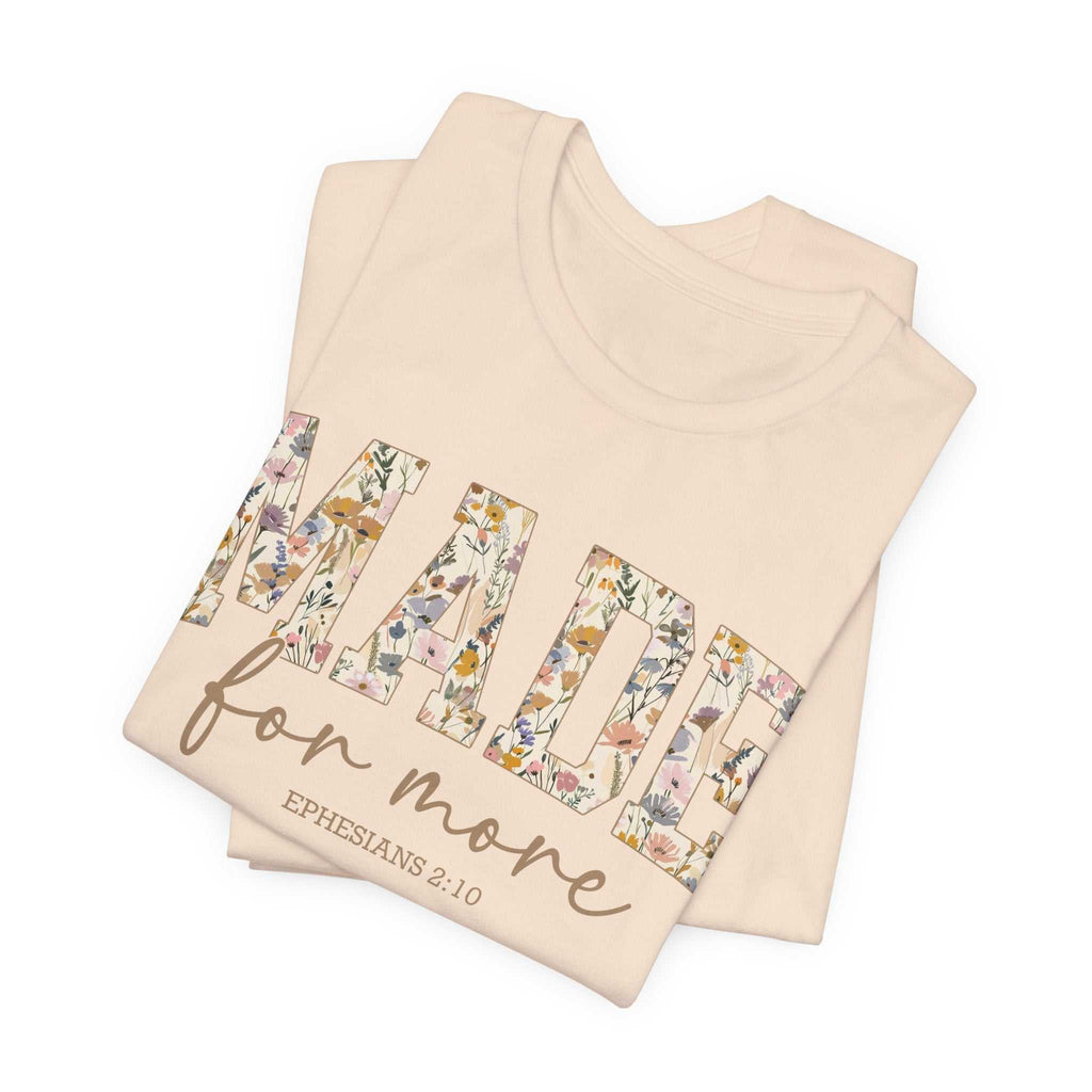 Folded beige "Made for More" unisex tee with floral text design and Ephesians 2:10 scripture reference, breathable cotton fabric.