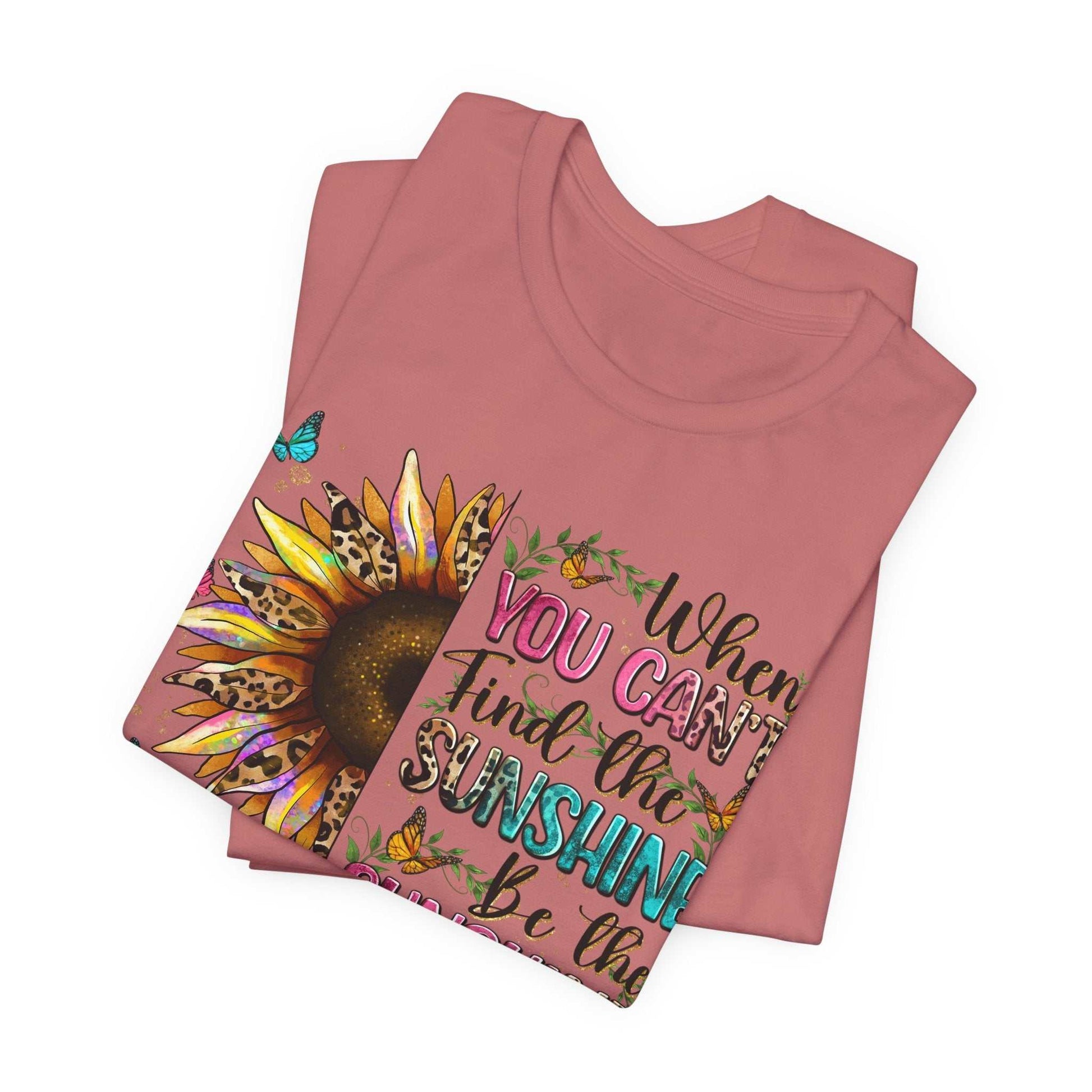 Folded pink Sunshine Quote Tee with colorful sunflower and motivational text design.