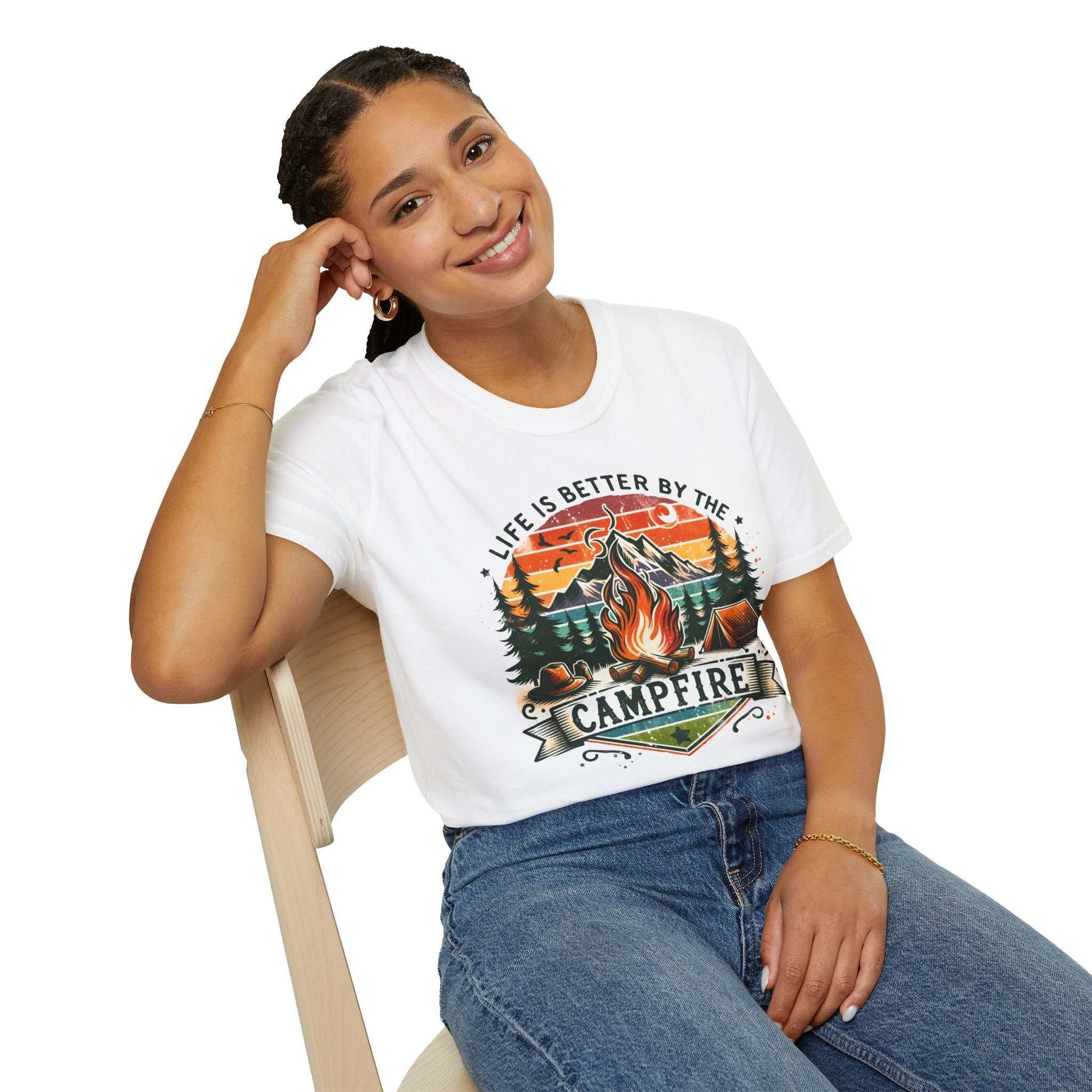 Woman wearing white Camping Adventure Unisex T-Shirt with "Life is Better by the Campfire" design sitting on chair