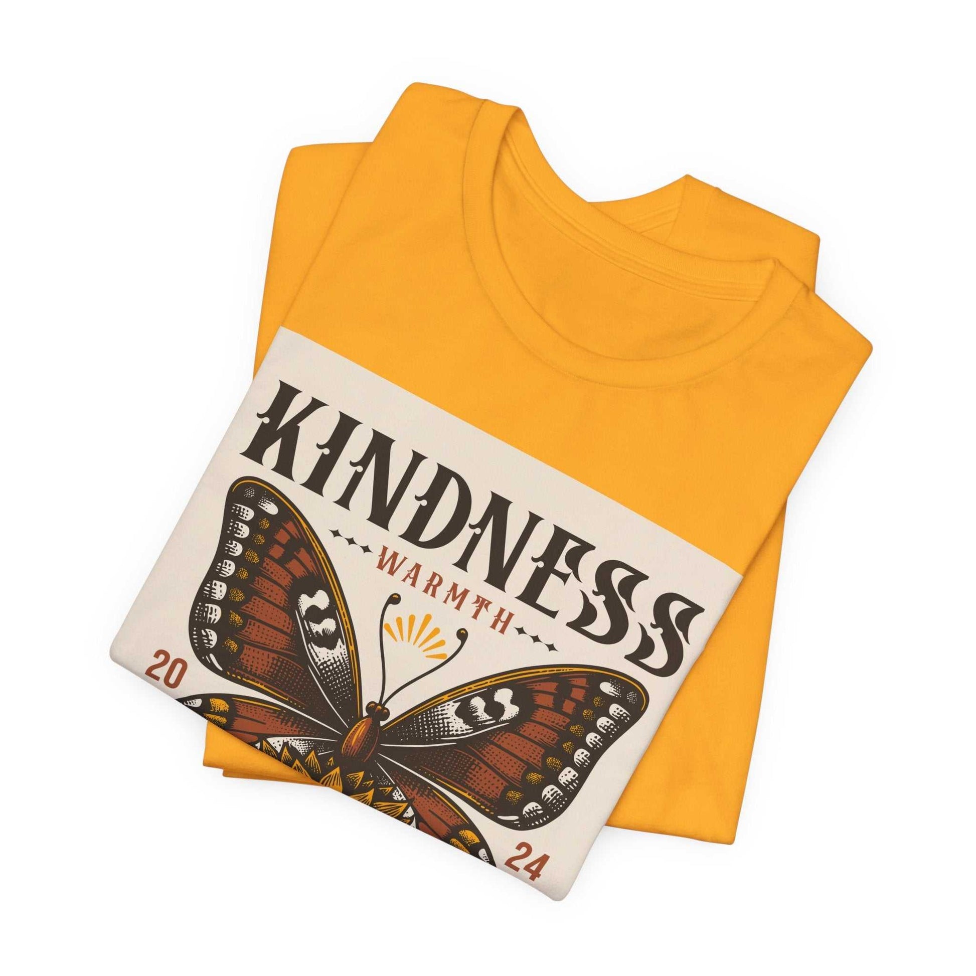 Folded yellow Kindness Butterfly Tee featuring a butterfly graphic with the word "Kindness" and "Warmth" printed on the front