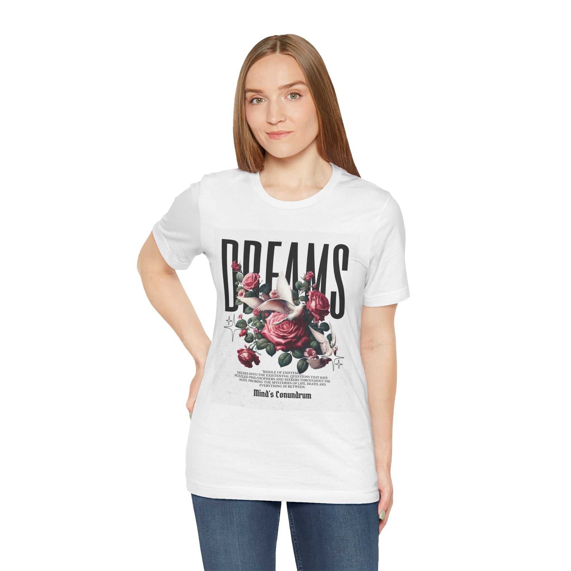Woman wearing white Dreams Floral Tee with bold black text and pink rose graphic on front, paired with blue jeans.