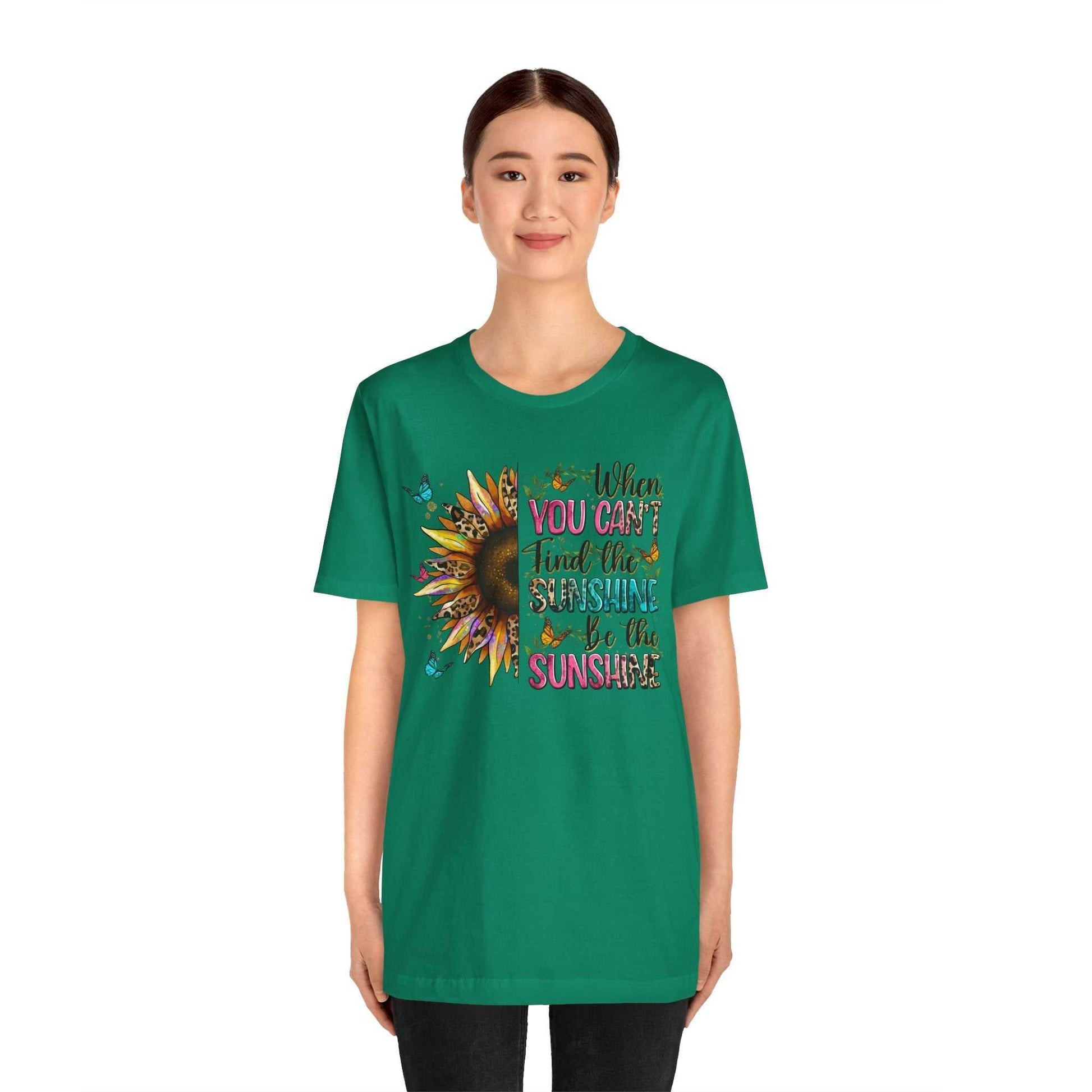 Woman wearing green Sunshine Quote Tee with sunflower design and inspirational text "When you can't find the sunshine be the sunshine"
