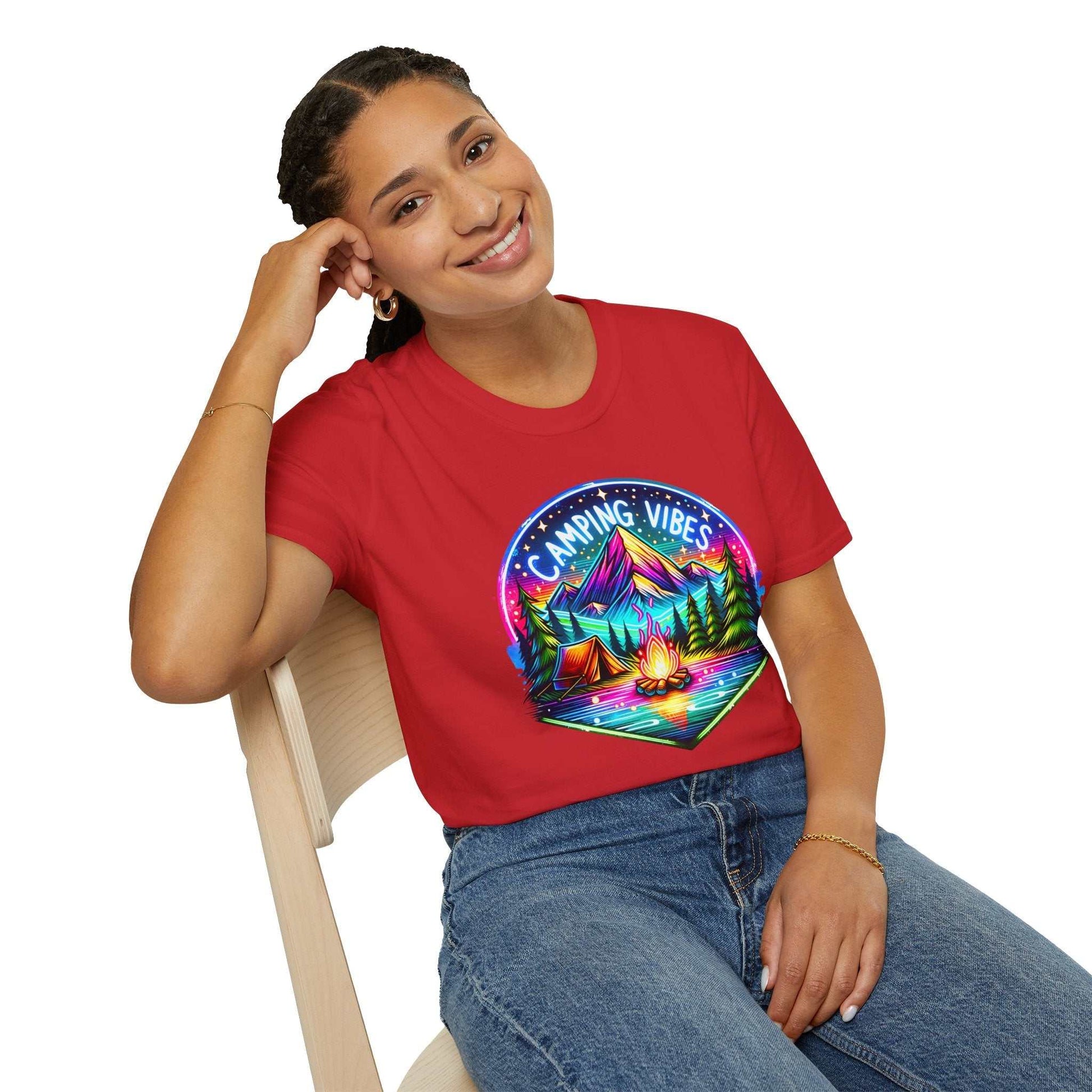 Woman wearing red Camping Vibes Unisex softstyle t-shirt with colorful camping graphic sitting on chair smiling