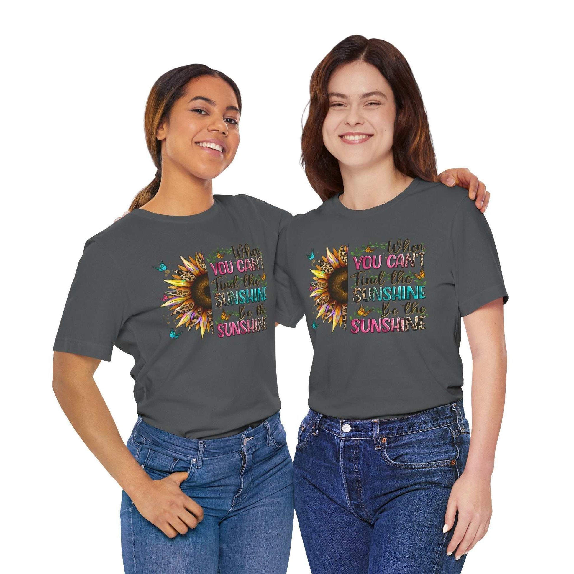 Two women wearing grey Sunshine Quote Tee with colorful sunflower and inspirational text design, styled casually with blue jeans