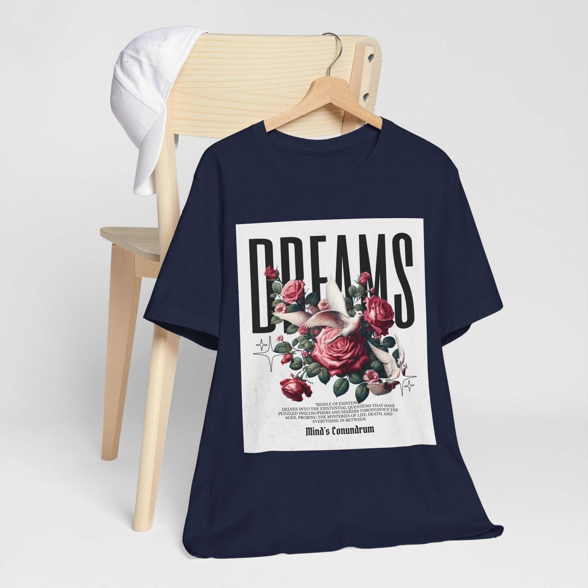Navy Dreams Floral Tee with rose and floral graphic on front, displayed hanging on wooden chair with white cap.