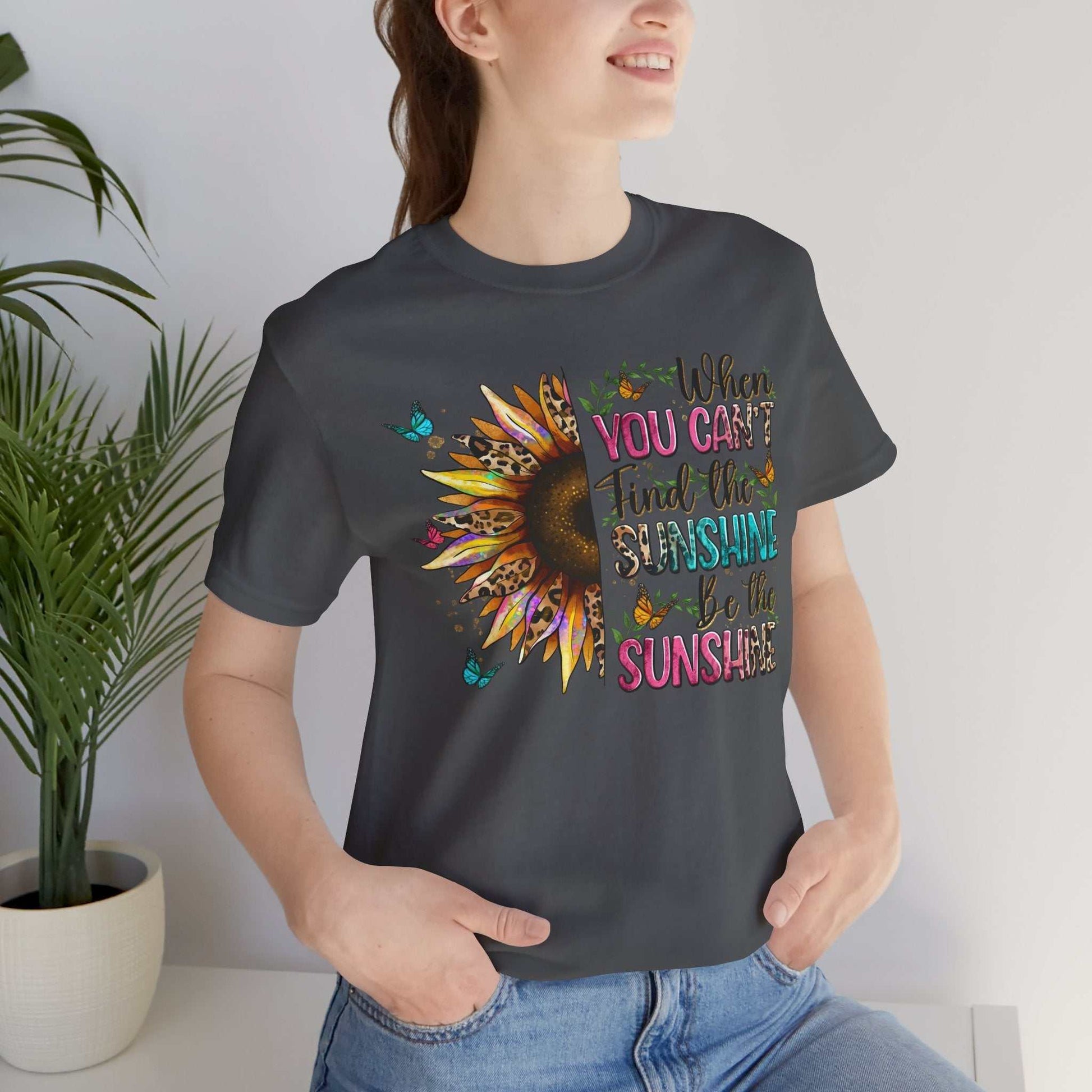Woman wearing a dark grey Sunshine Quote Tee with colorful sunflower and inspirational text design on front