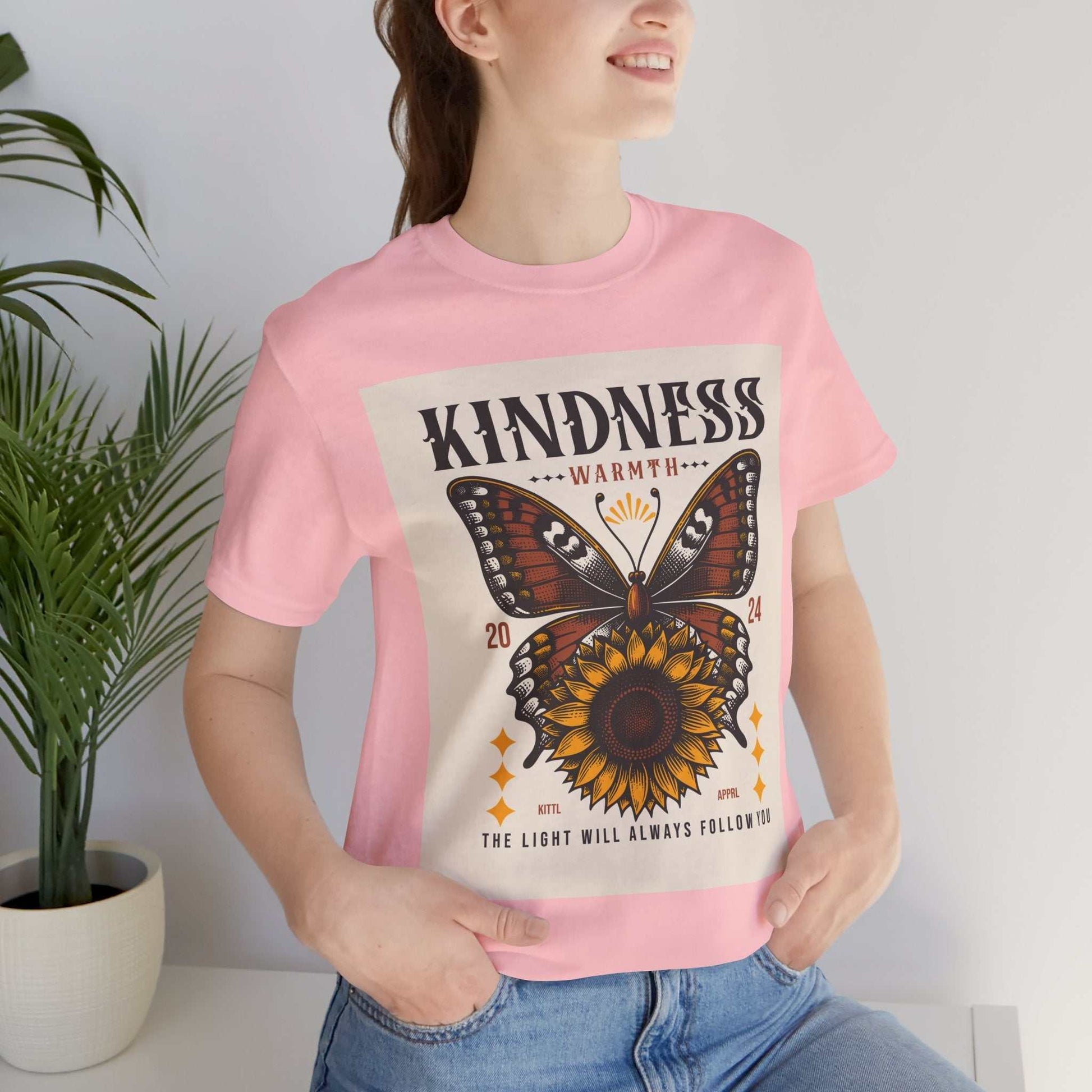 Woman wearing pink Kindness Butterfly Tee with butterfly and sunflower graphic design on front