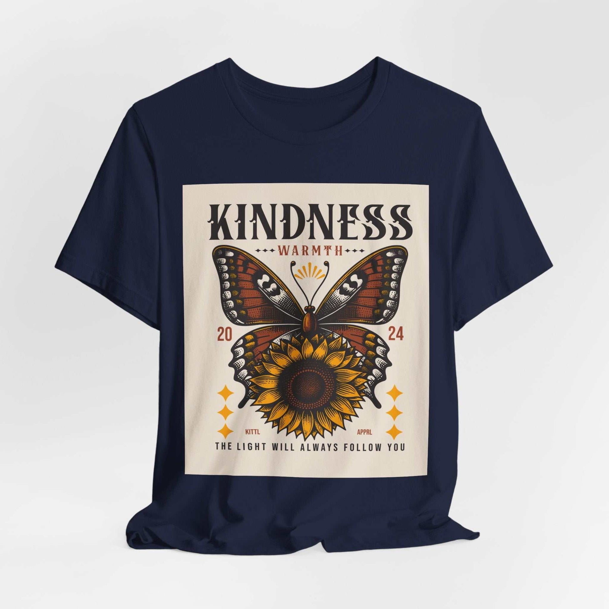 Navy t-shirt with a butterfly and sunflower design featuring the text "Kindness Warmth 2024" and "The light will always follow you"