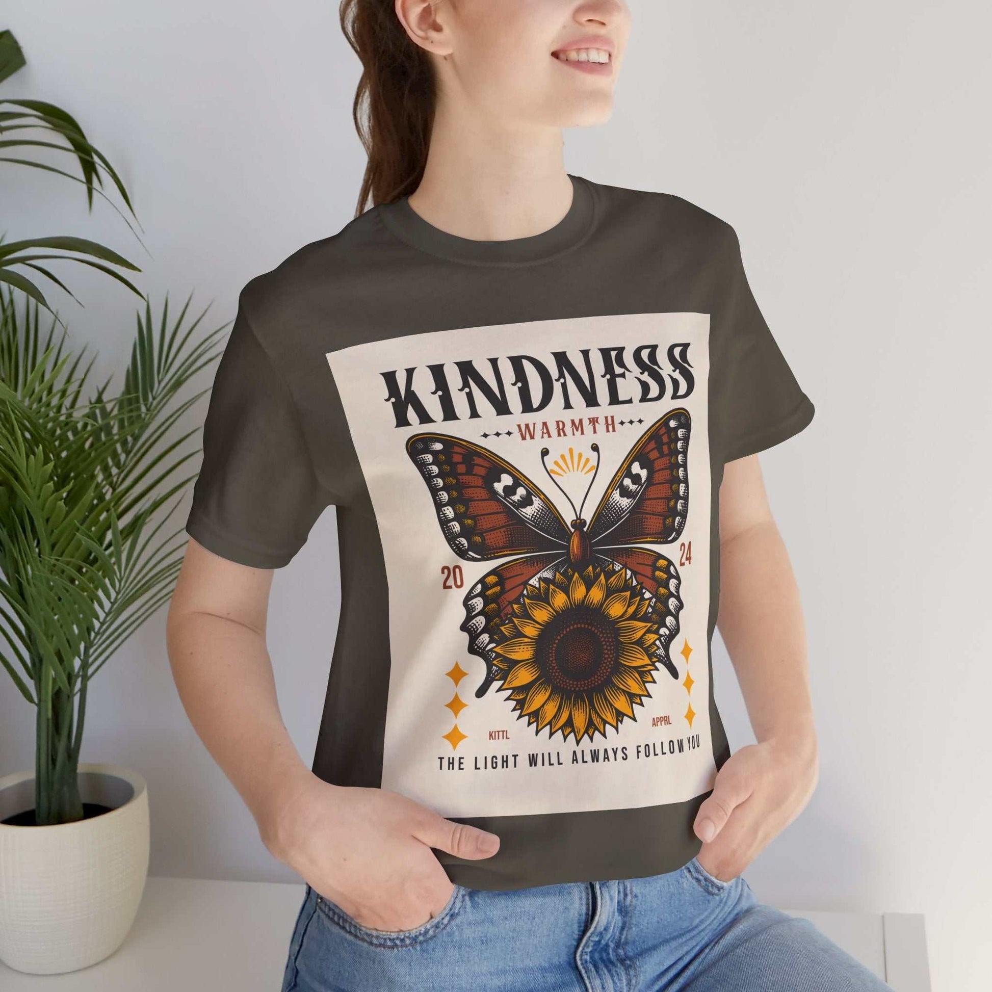 Woman wearing a Kindness Butterfly Tee with a butterfly and sunflower design and the text "Kindness Warmth 2024 The light will always follow you" on a dark short sleeve t-shirt.