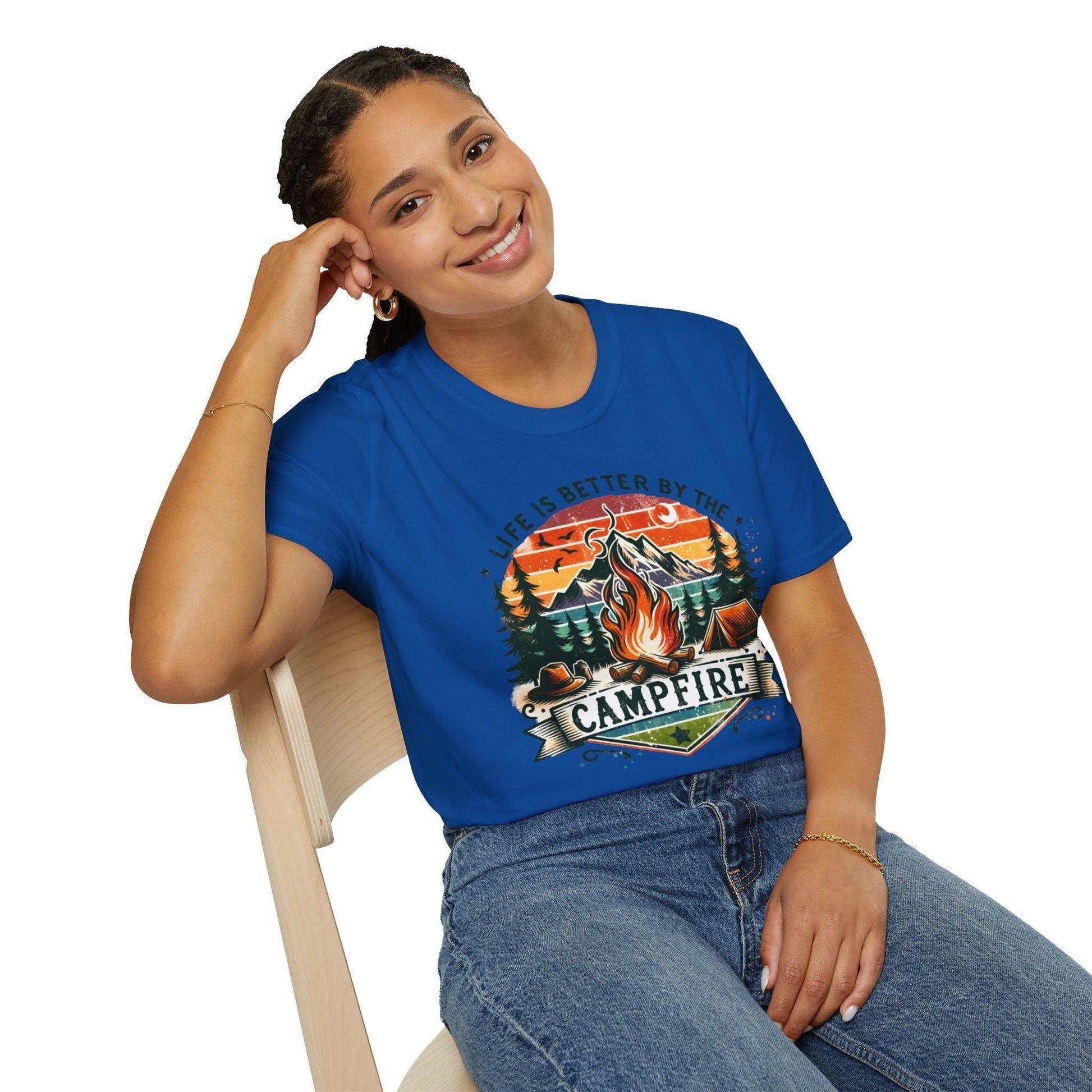 Woman wearing blue Camping Adventure unisex t-shirt with campfire graphic and "Life is Better by the Campfire" text sitting on chair