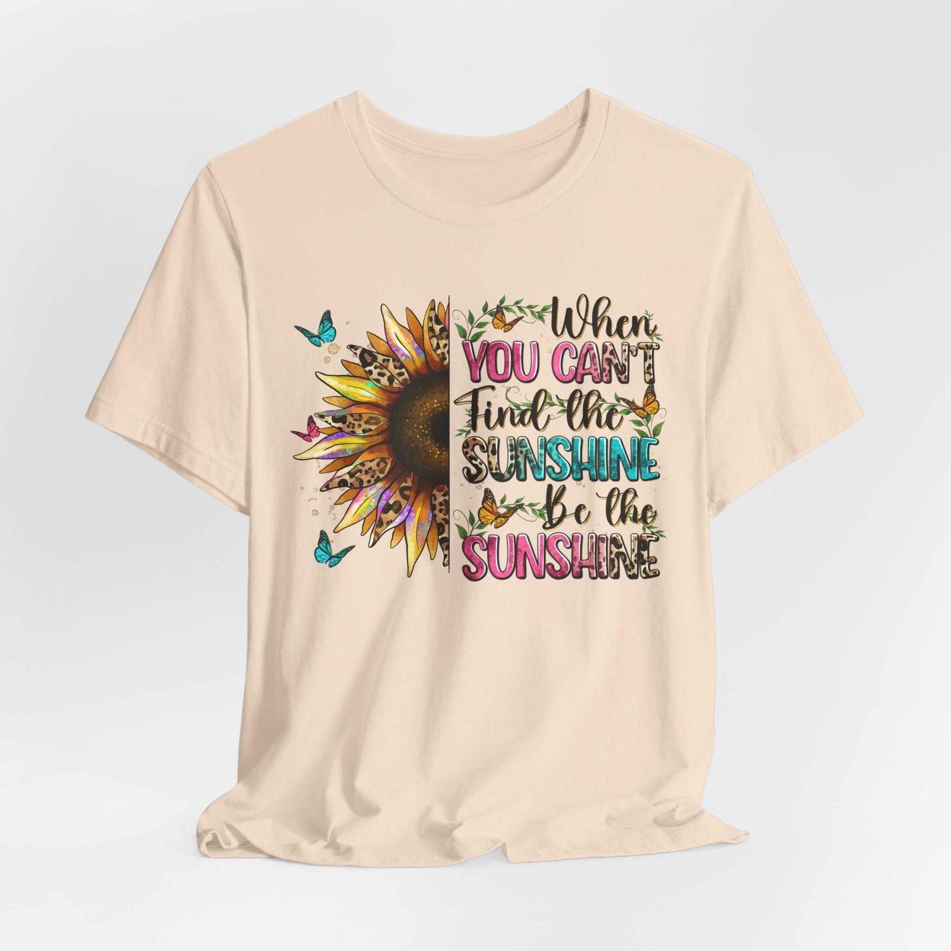 Beige Sunshine Quote Tee with colorful sunflower, butterflies, and inspirational text "When you can't find the sunshine be the sunshine" printed on front.