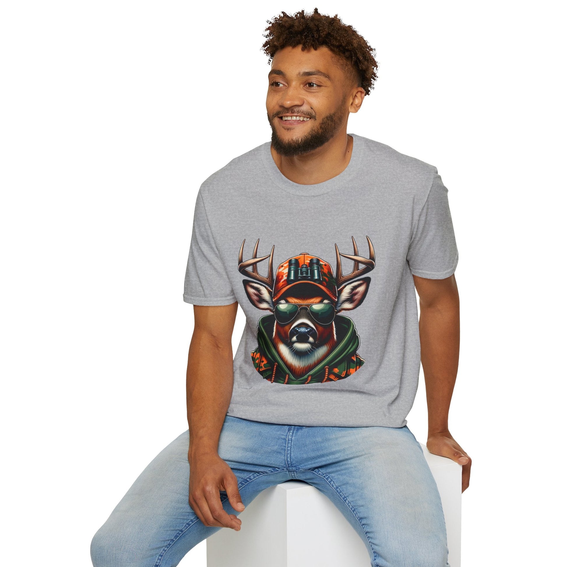 Man wearing a gray hunting enthusiast t-shirt with a graphic of a deer wearing sunglasses and a camouflage hat sitting on a white block