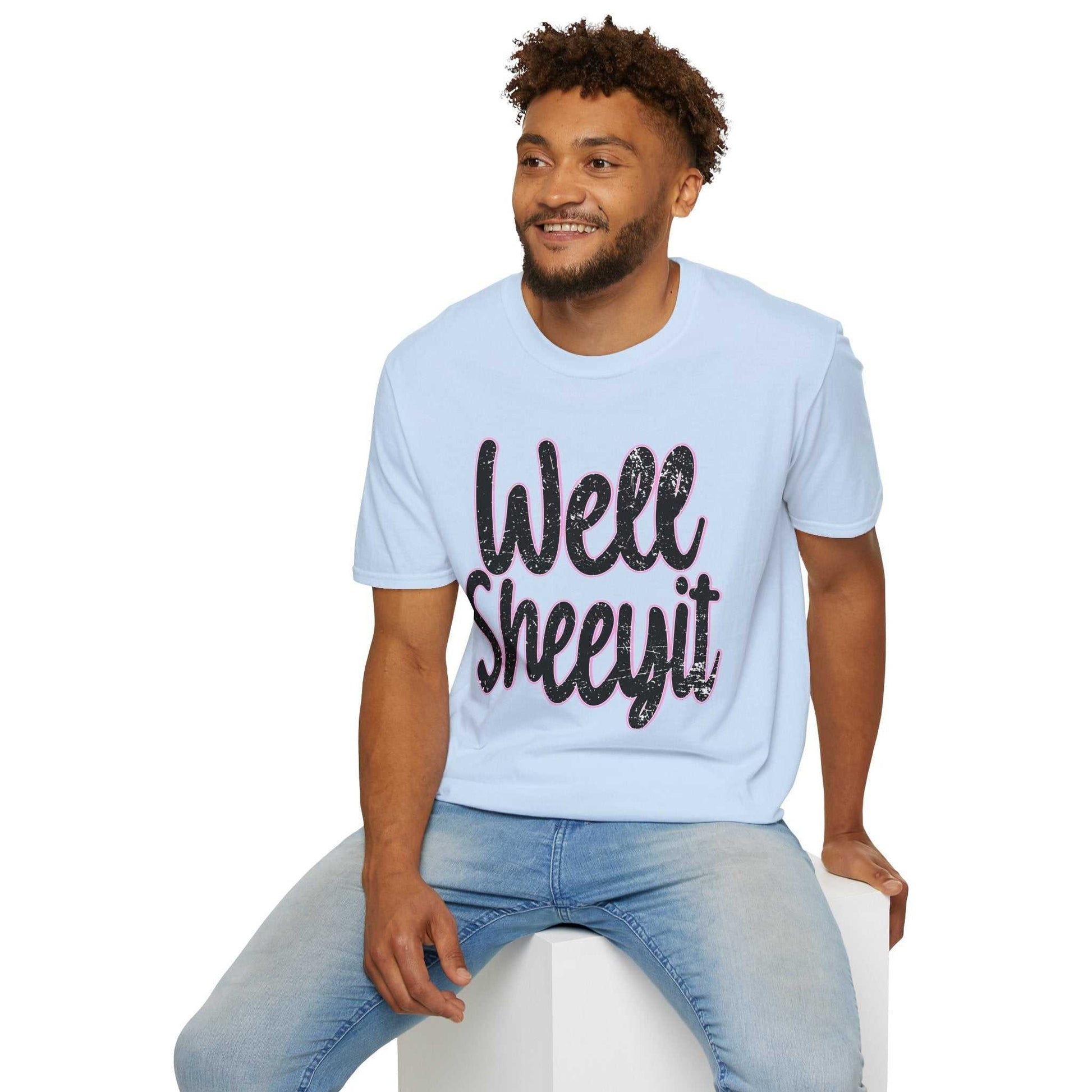 Man wearing light blue casual statement tee with "Well Sheeyit" funny quote sitting on white block