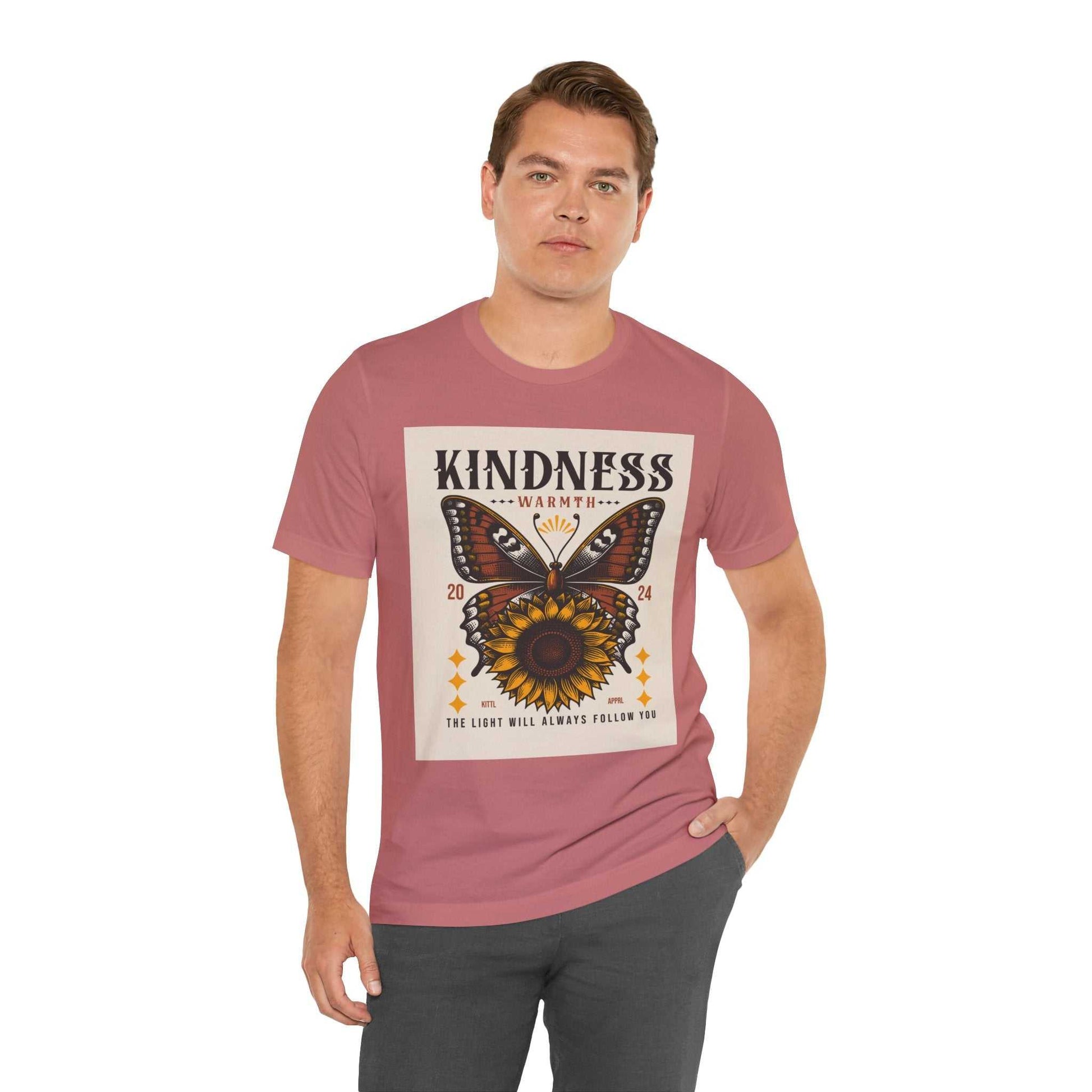 Man wearing a pink Kindness Butterfly Tee with a butterfly and sunflower design and the text "Kindness Warmth 2024 The light will always follow you"