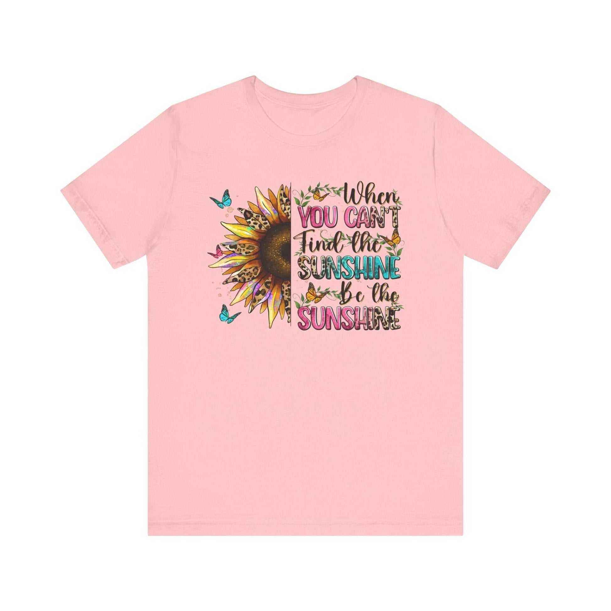 Pink unisex t-shirt with a vibrant sunflower and butterfly design featuring the quote "When you can't find the sunshine be the sunshine"