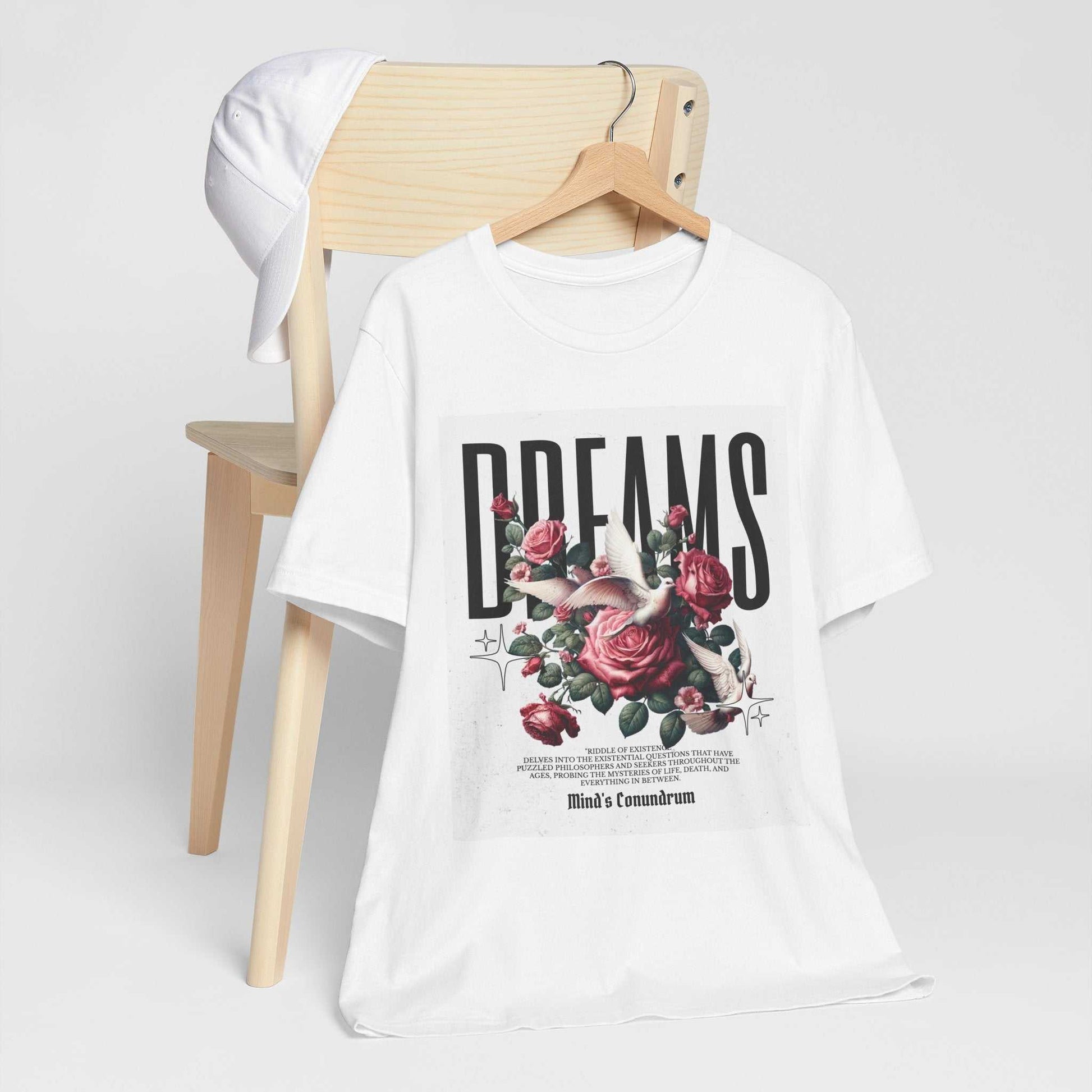 White Dreams Floral Tee with bold typography and pink rose graphic hanging on wooden chair with white cap