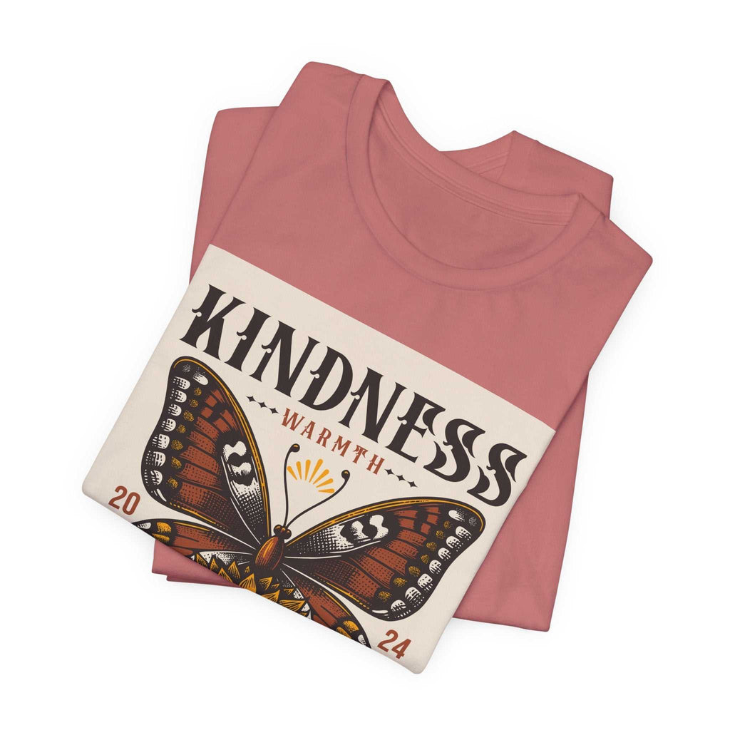 Folded rose pink Kindness Butterfly Tee with butterfly and sunflower design and "Kindness Warmth" text.