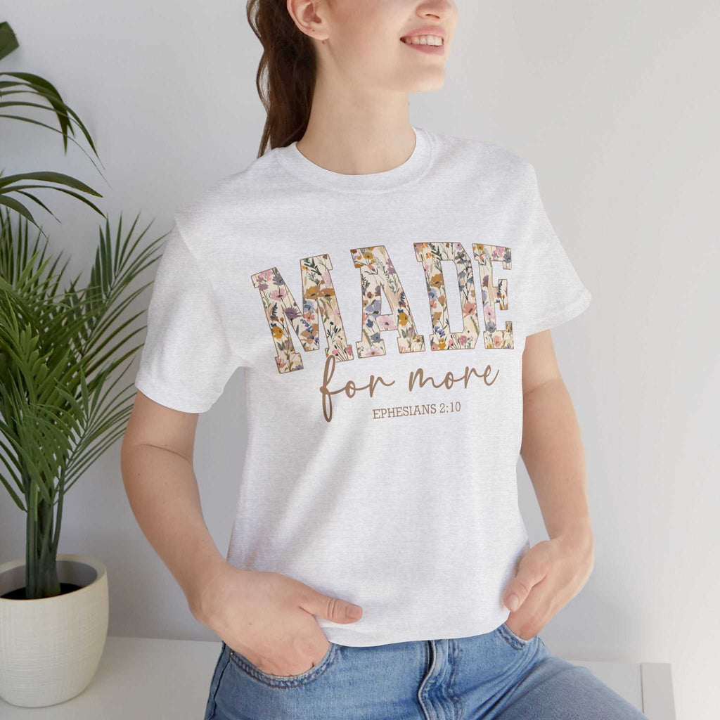 Woman wearing a white Made for More Tee with floral text design and Ephesians 2:10 scripture, paired with blue jeans.