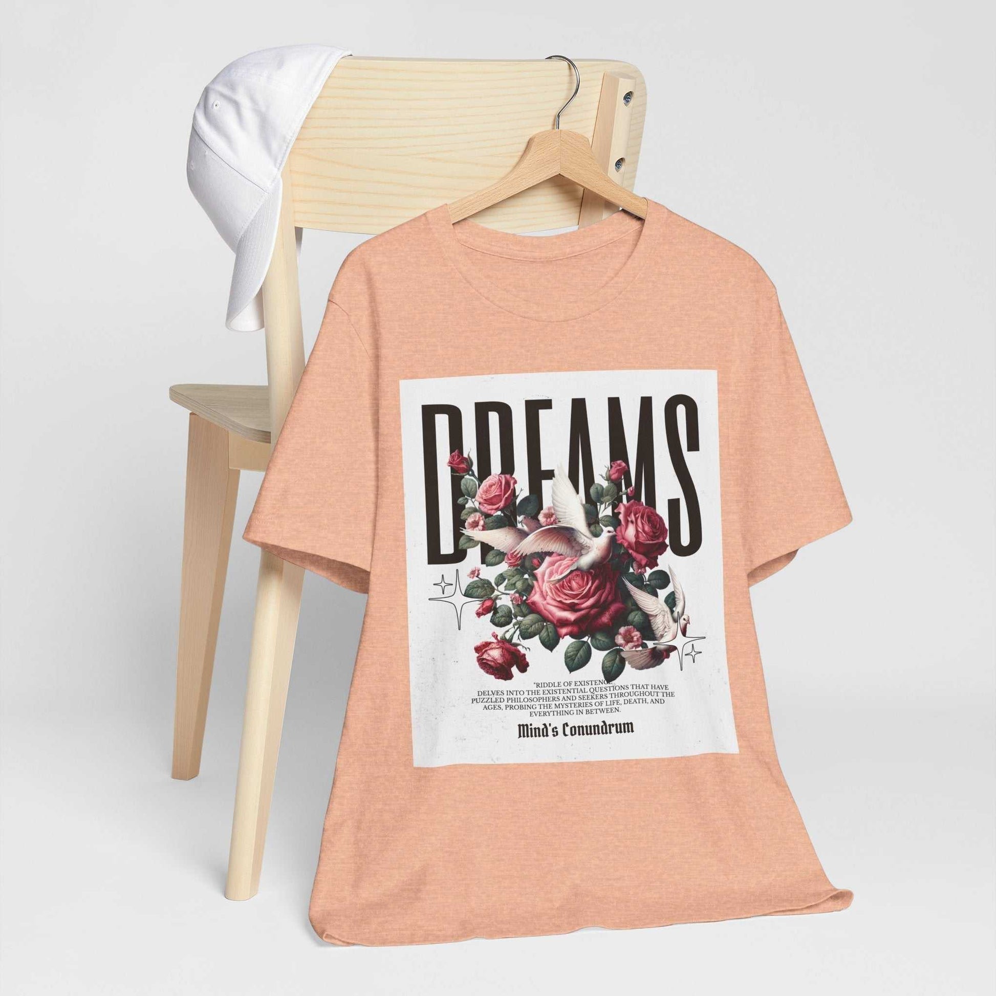 Peach Dreams Floral Tee with bold typography and rose flower design on front, displayed on wooden chair with white cap.