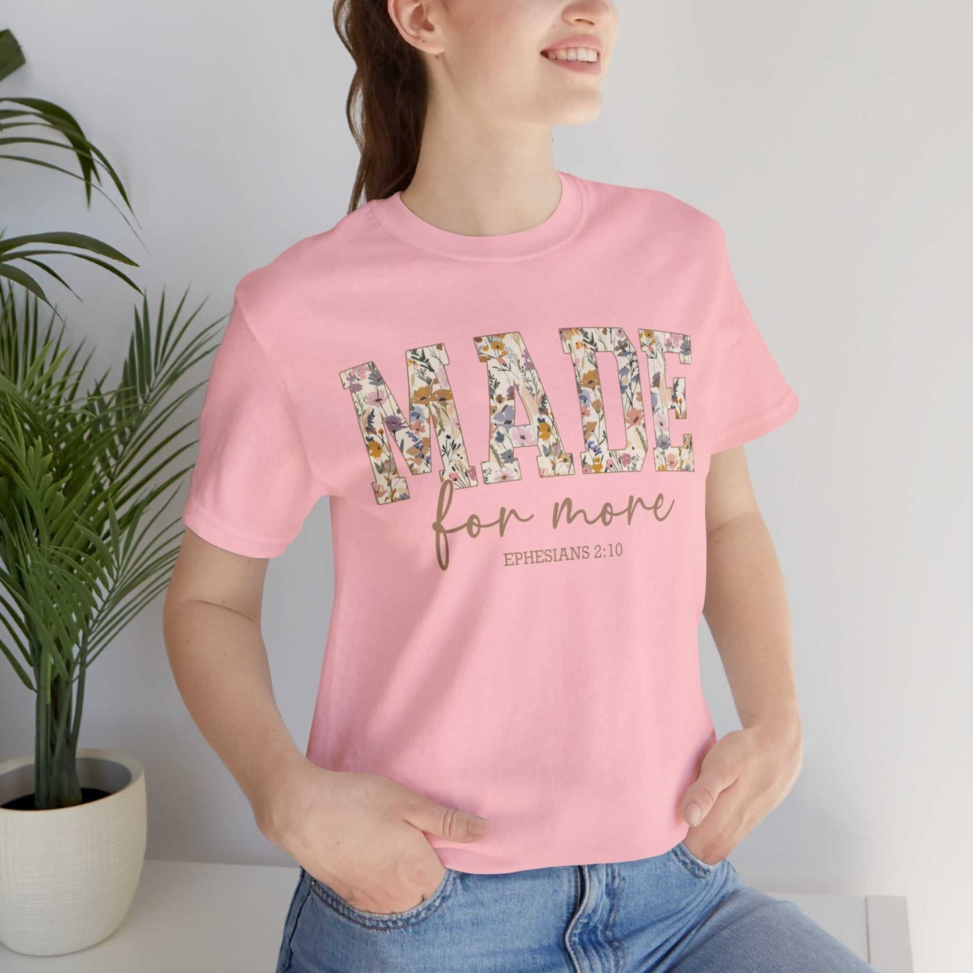 Woman wearing pink "Made for More" floral print tee shirt with Ephesians 2:10 scripture text.